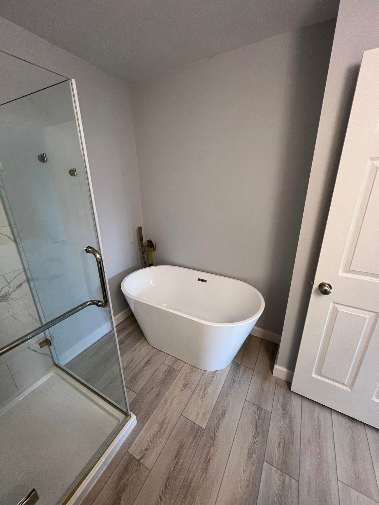 Modern bathroom with freestanding oval bathtub, glass shower, and light wood-look flooring.