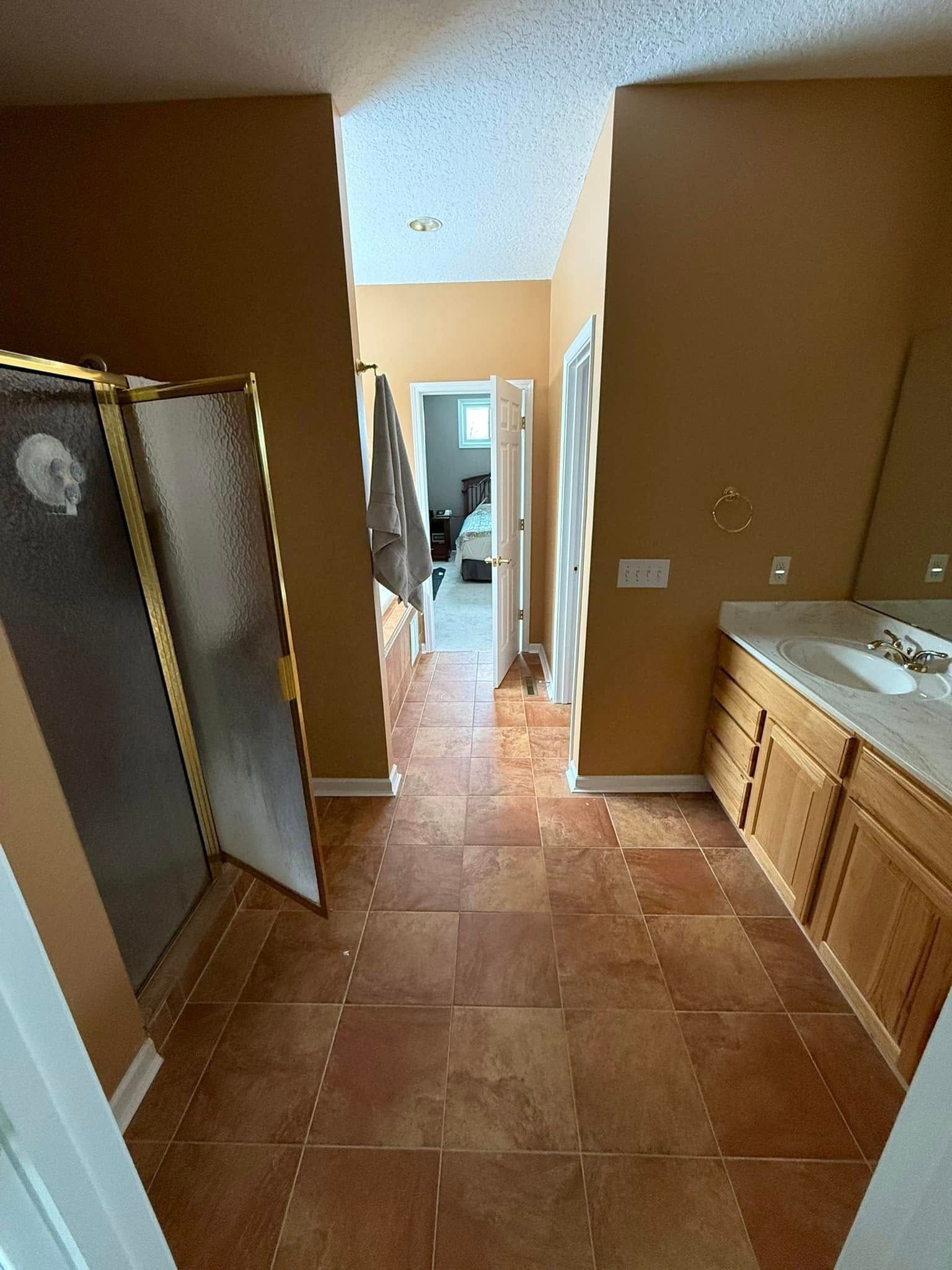 Bathroom with brown tiled floor, light brown walls, and vanity. View to bedroom.