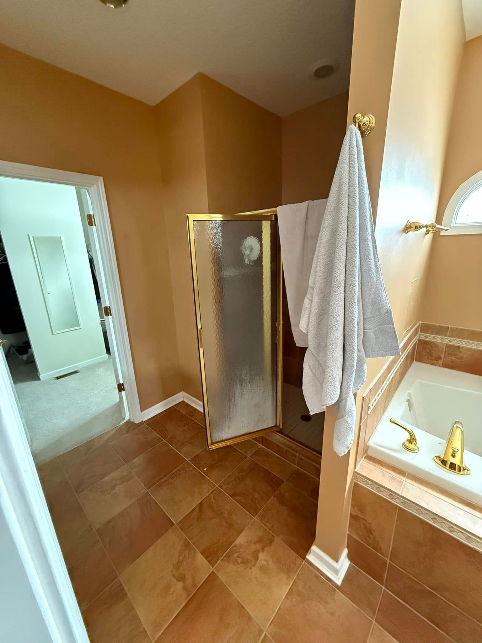 Bathroom with gold fixtures, shower, and towel. Earth-tone colors, tile floor, and a doorway.