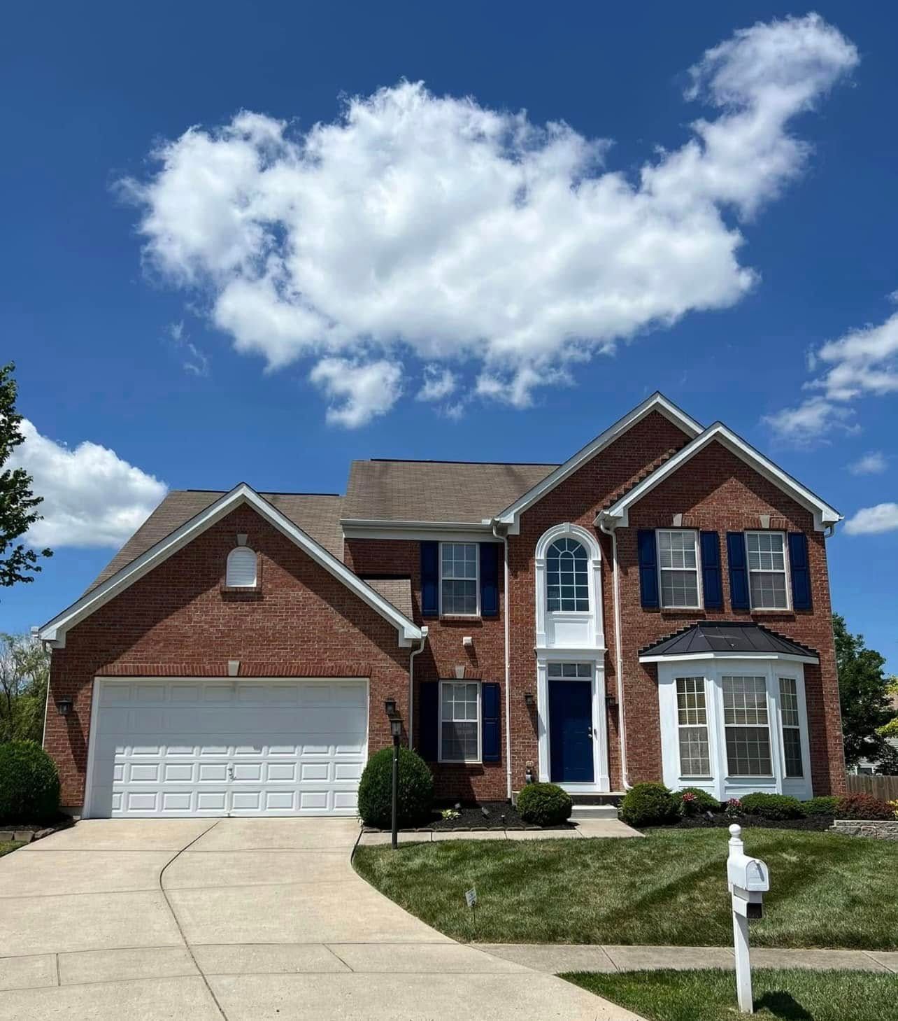 Brick two-story house with white garage door, blue shutters, and a blue front door under a partly cloudy blue sky.