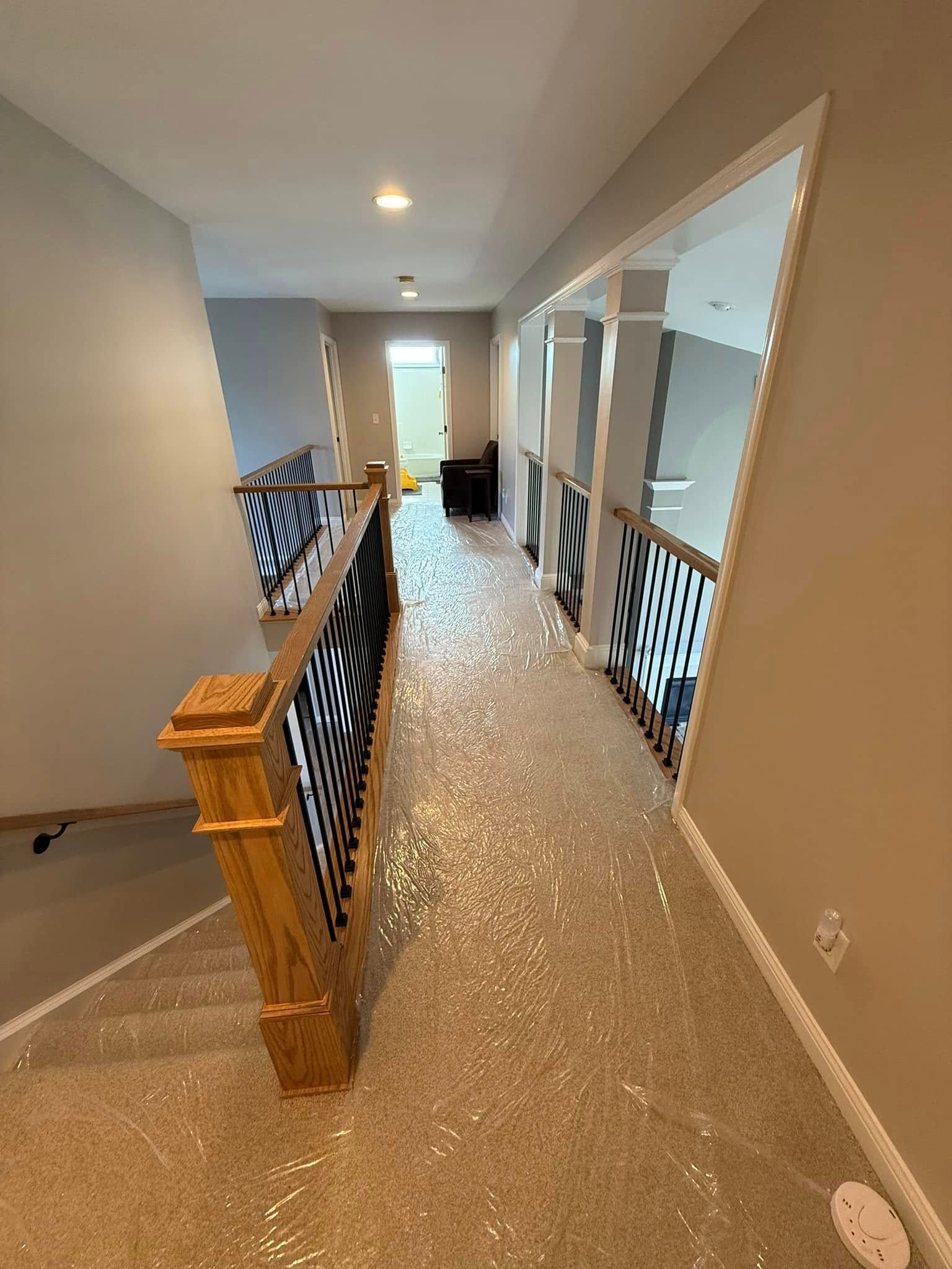 Hallway with a wooden banister with black and white decorative panels. Carpeted floor covered in plastic.