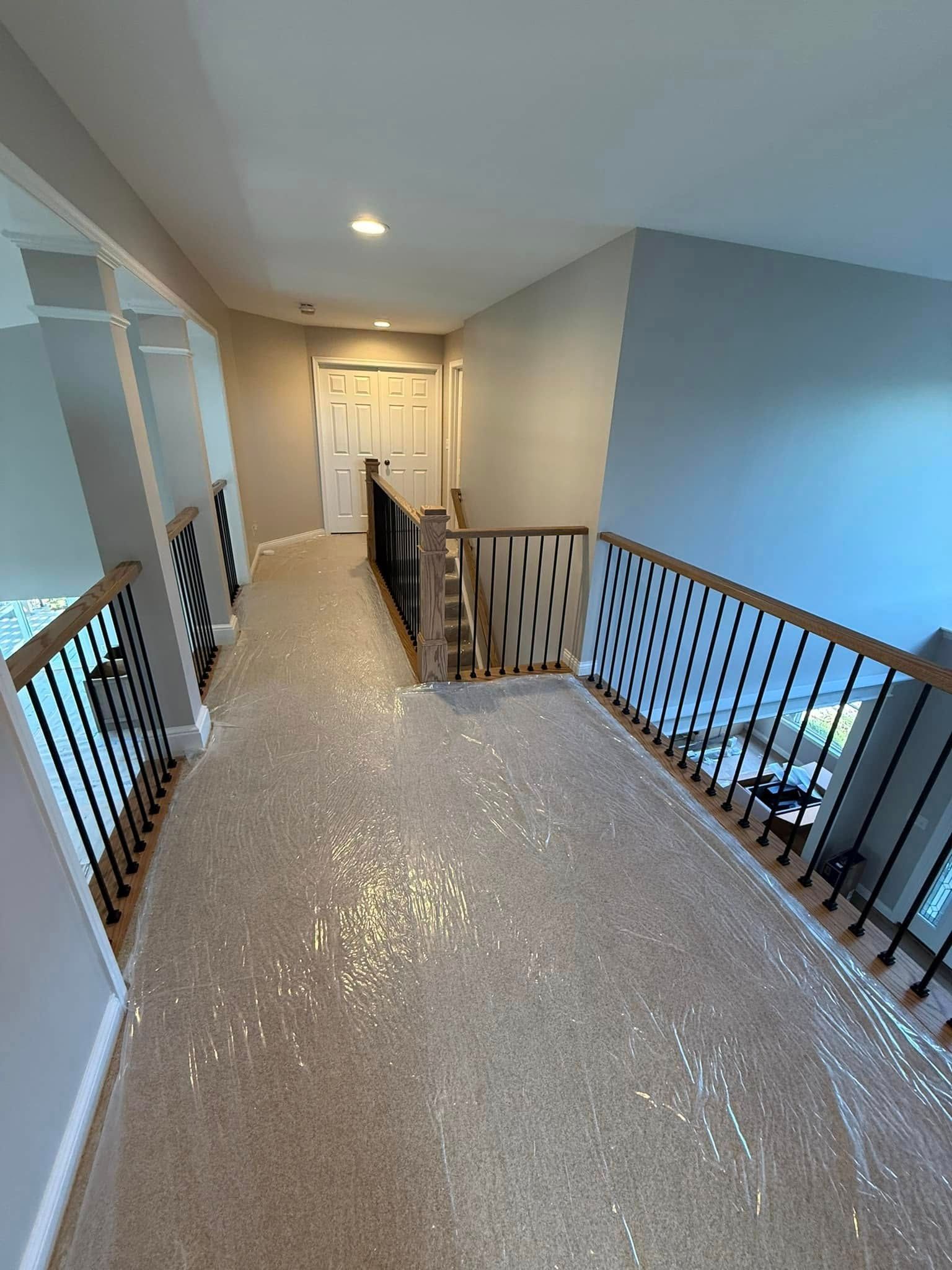 Hallway with carpeted floor, light gray walls, dark handrails, and a doorway at the end.