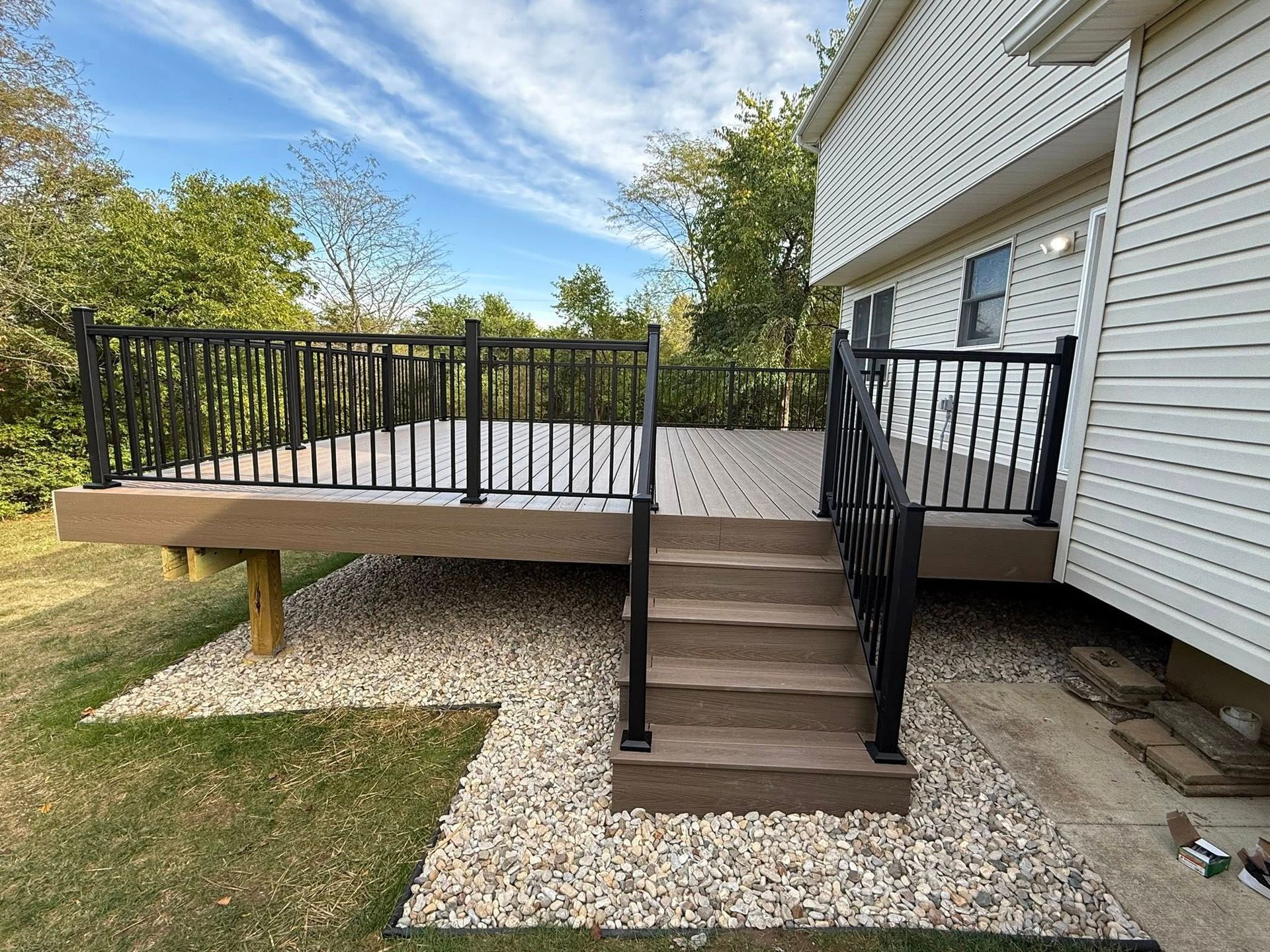 Composite deck with black railing and steps leading to it, gravel bed beneath.