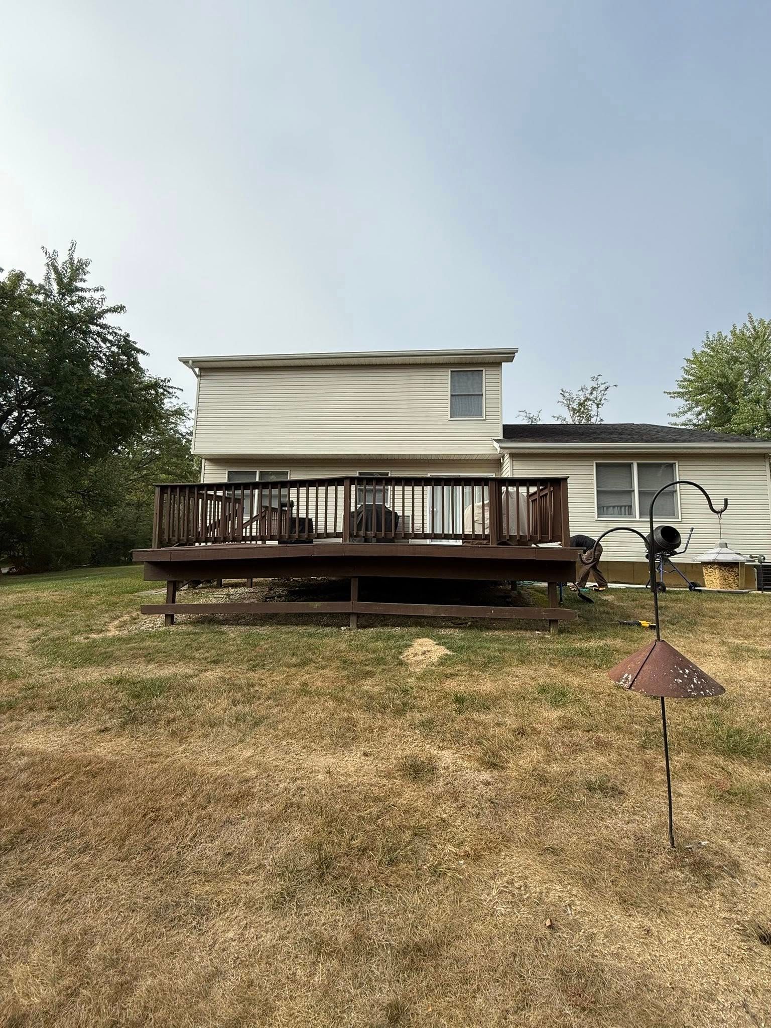 Backyard view of a two-story beige house with a brown wooden deck, lawn in foreground, overcast sky.