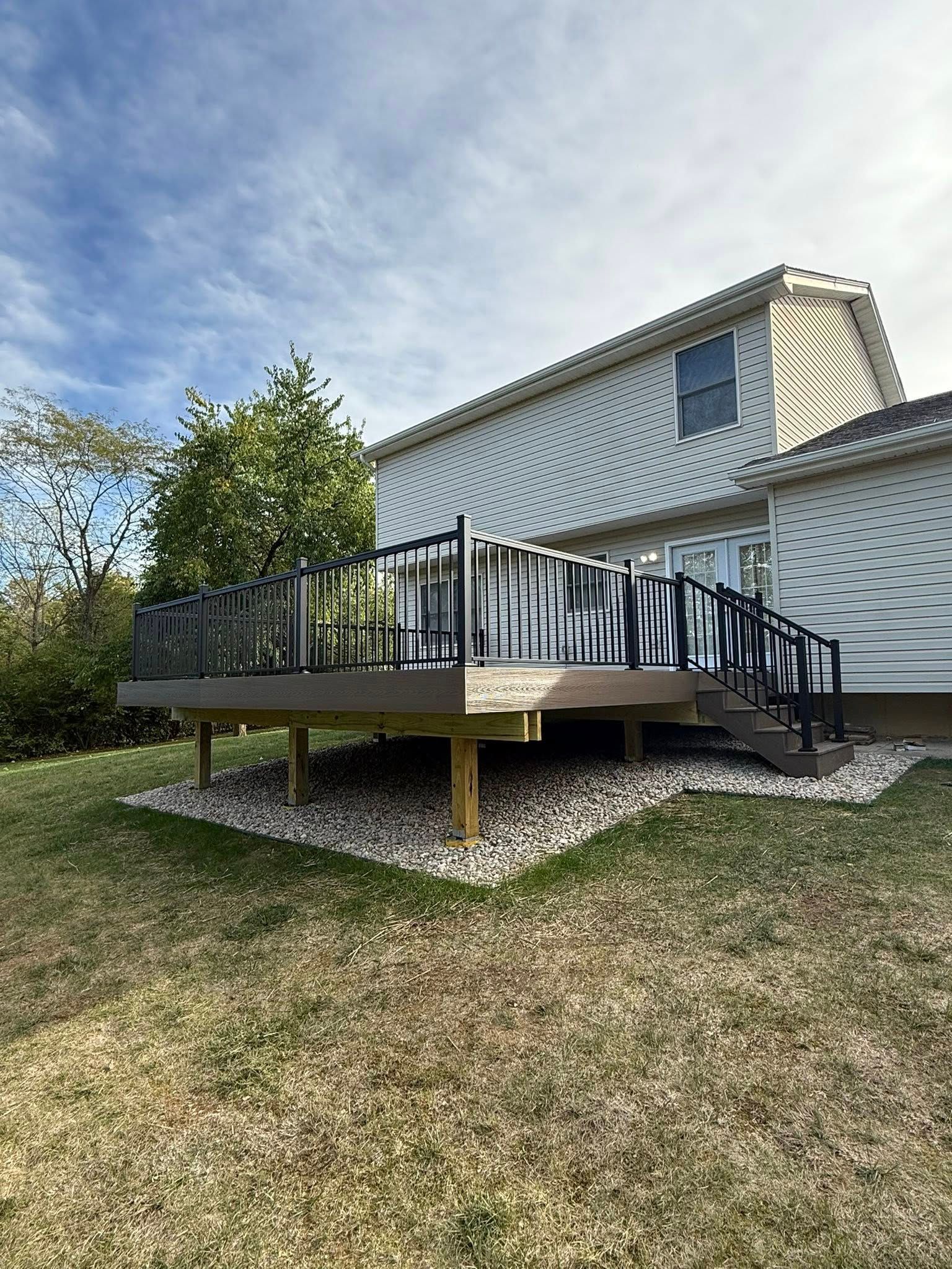 A deck with black railings and composite boards sits adjacent to a two-story house.