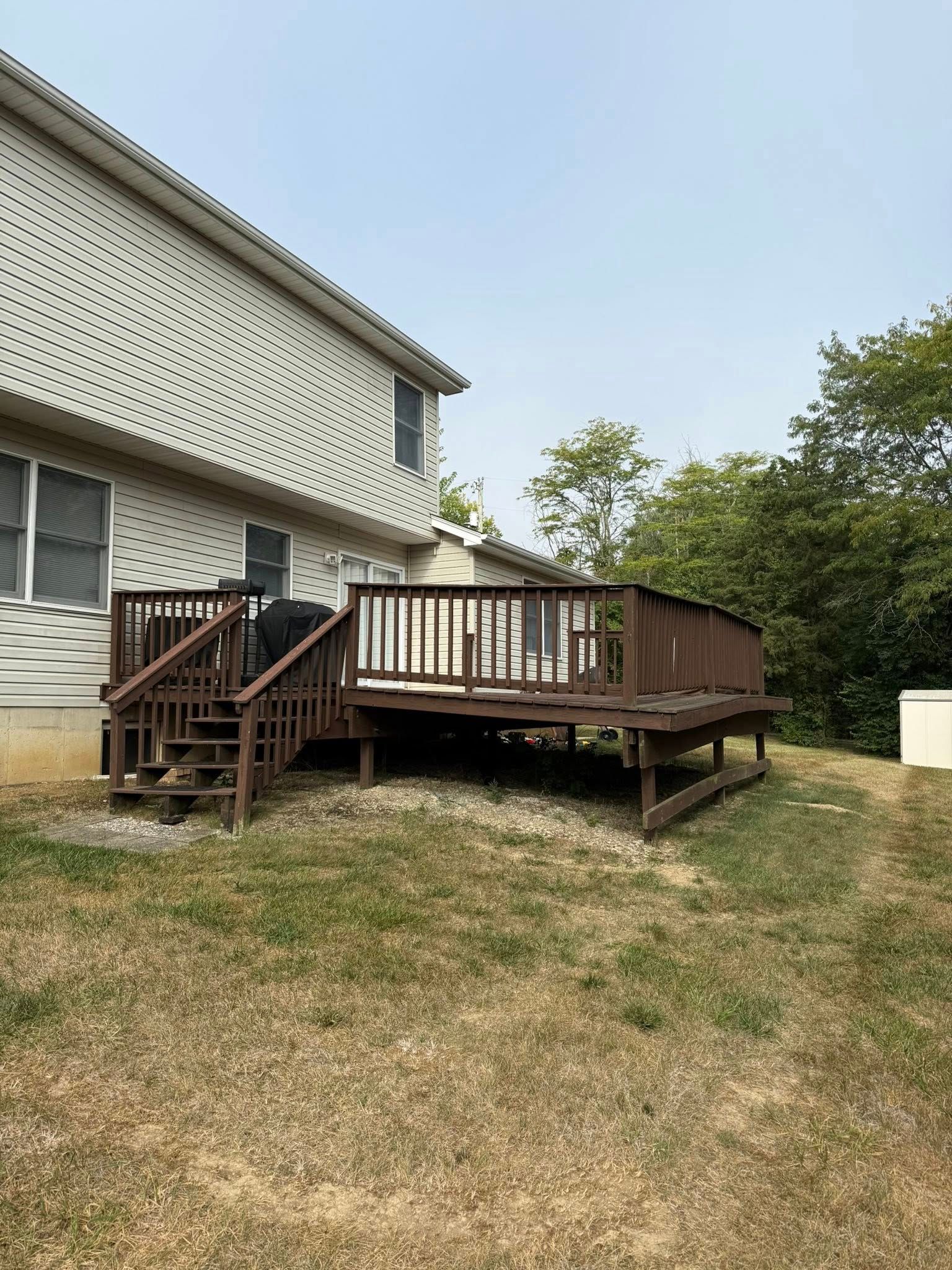 Wooden deck attached to a two-story beige house with steps leading down to a grassy yard.