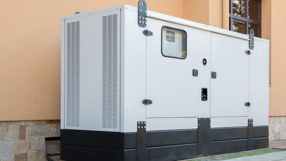 Large white industrial generator unit beside a building, with vents, black base, and a small access window.