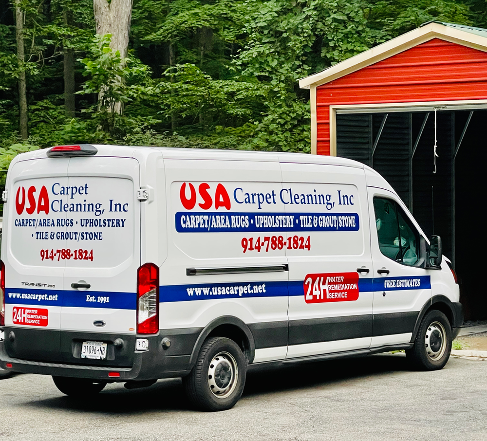 A usa carpet cleaning van is parked in front of a red garage.