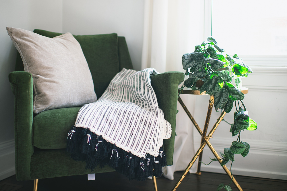 A green chair with a blanket on it and a plant on a table next to it.