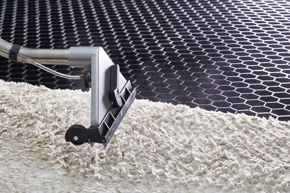 A vacuum cleaner is cleaning a carpet on a black tiled floor.