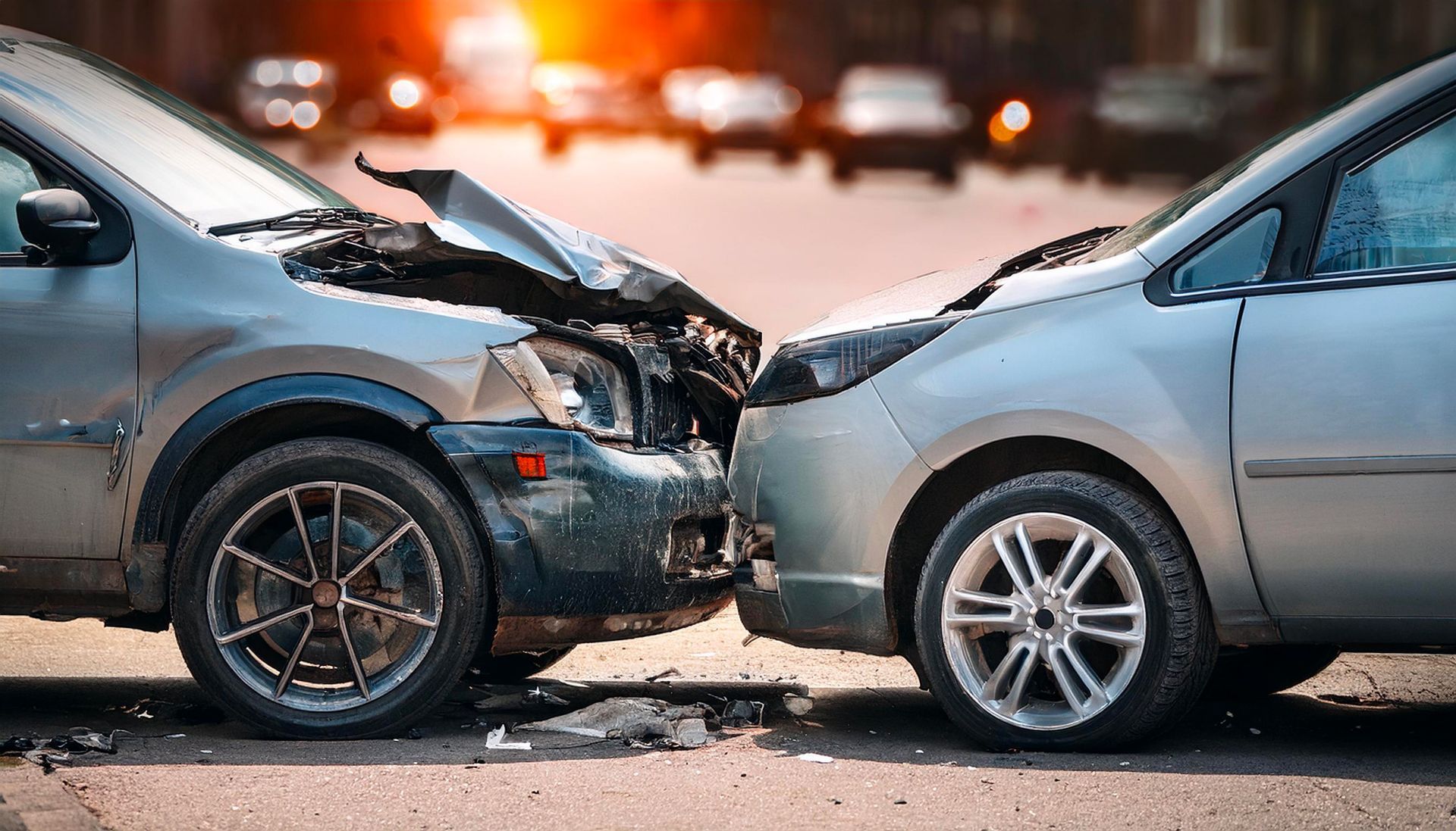 Two cars collide head-on on a road, with front ends crumpled and debris scattered.