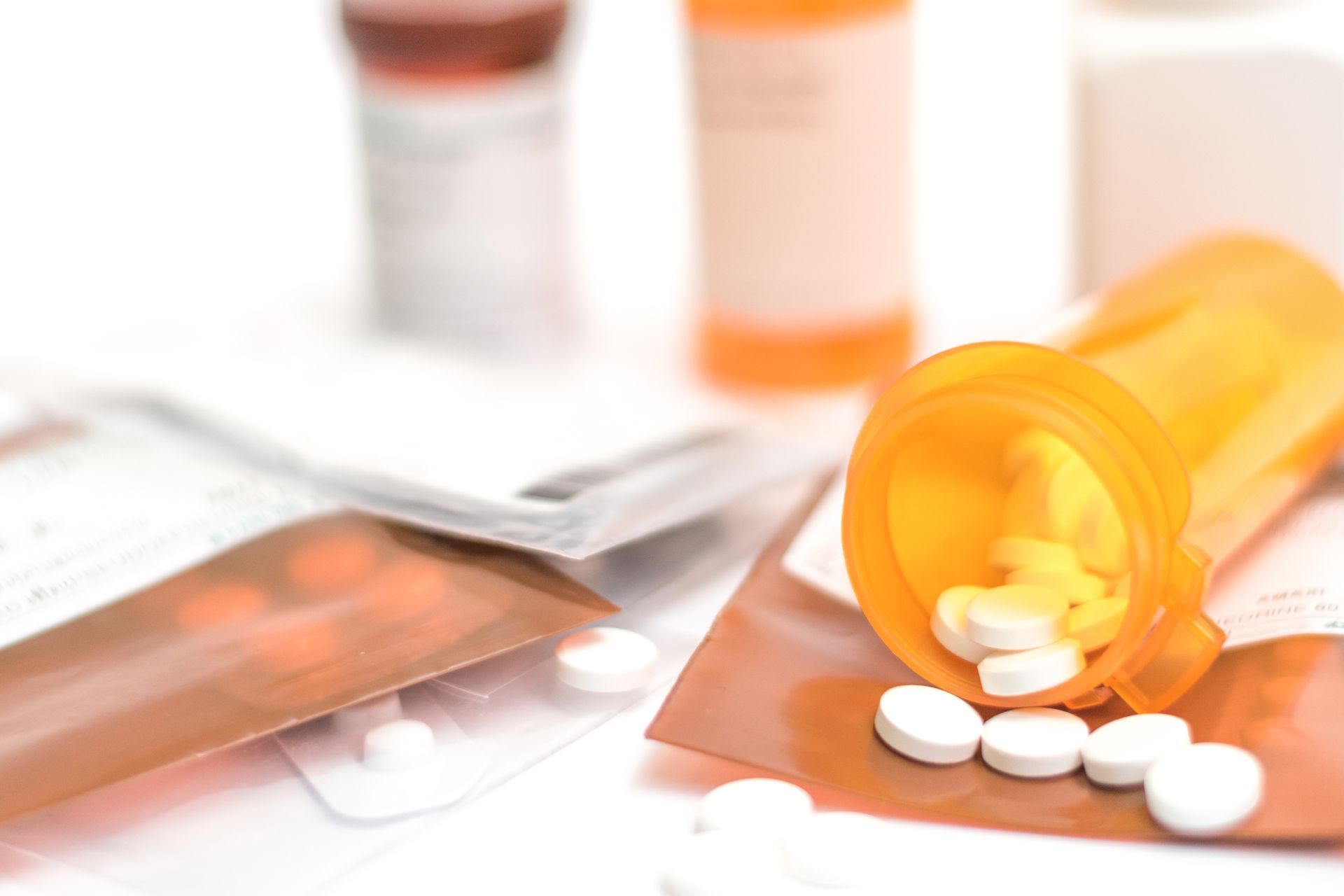 Orange prescription bottle spilling white pills beside medication packets and bottles on a white surface