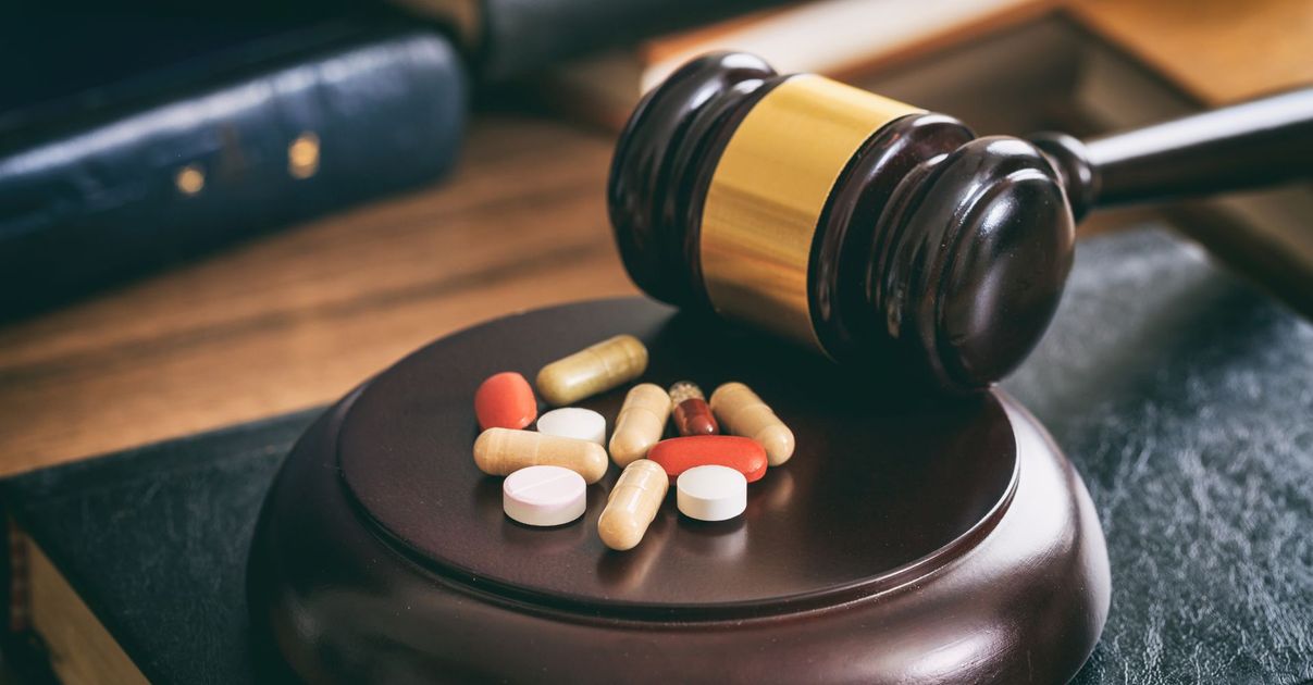 Judge’s gavel beside assorted pills on a wooden desk, suggesting legal issues around medication