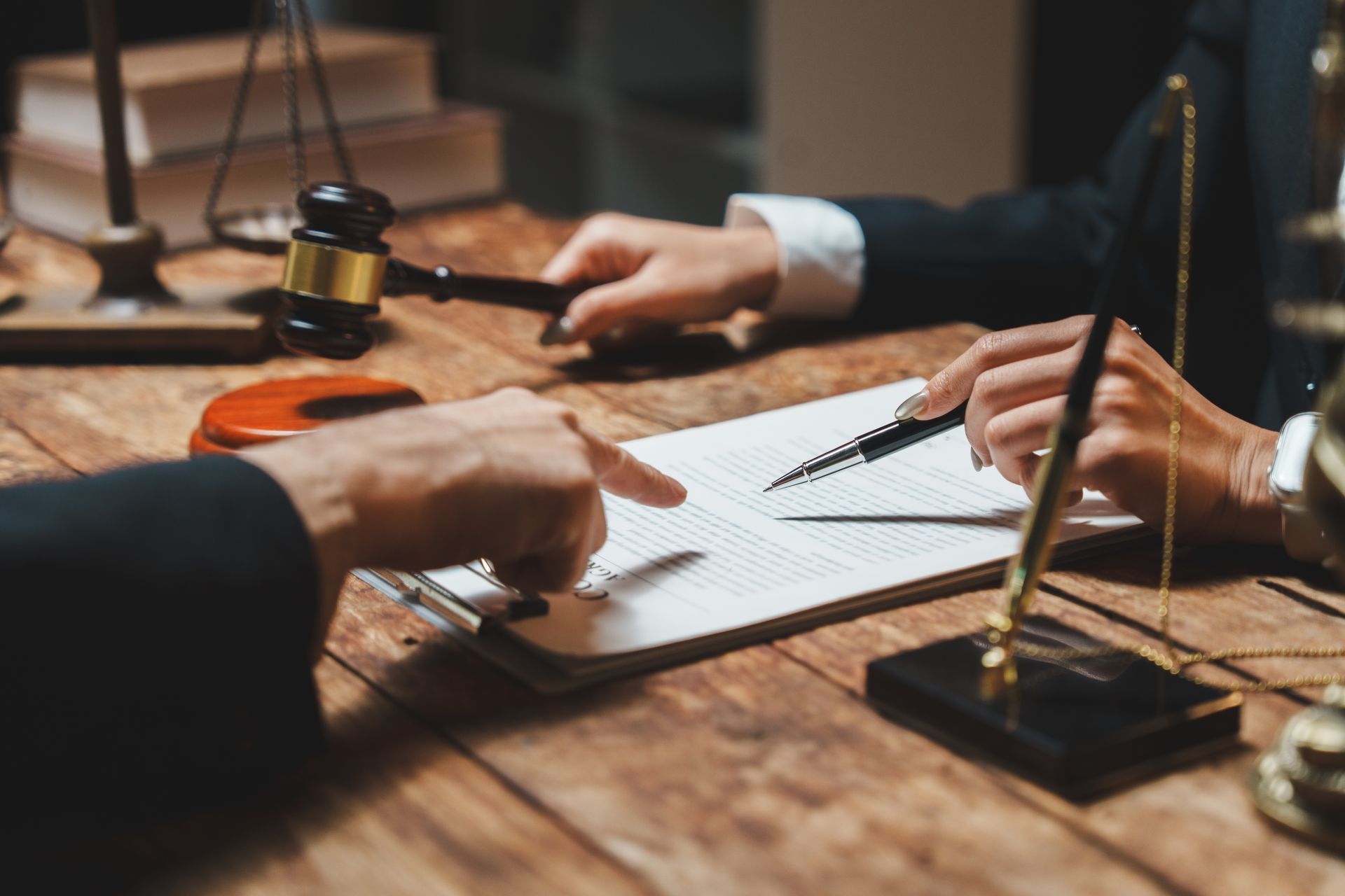 Hands signing a document with a gavel on a wooden desk in a legal office