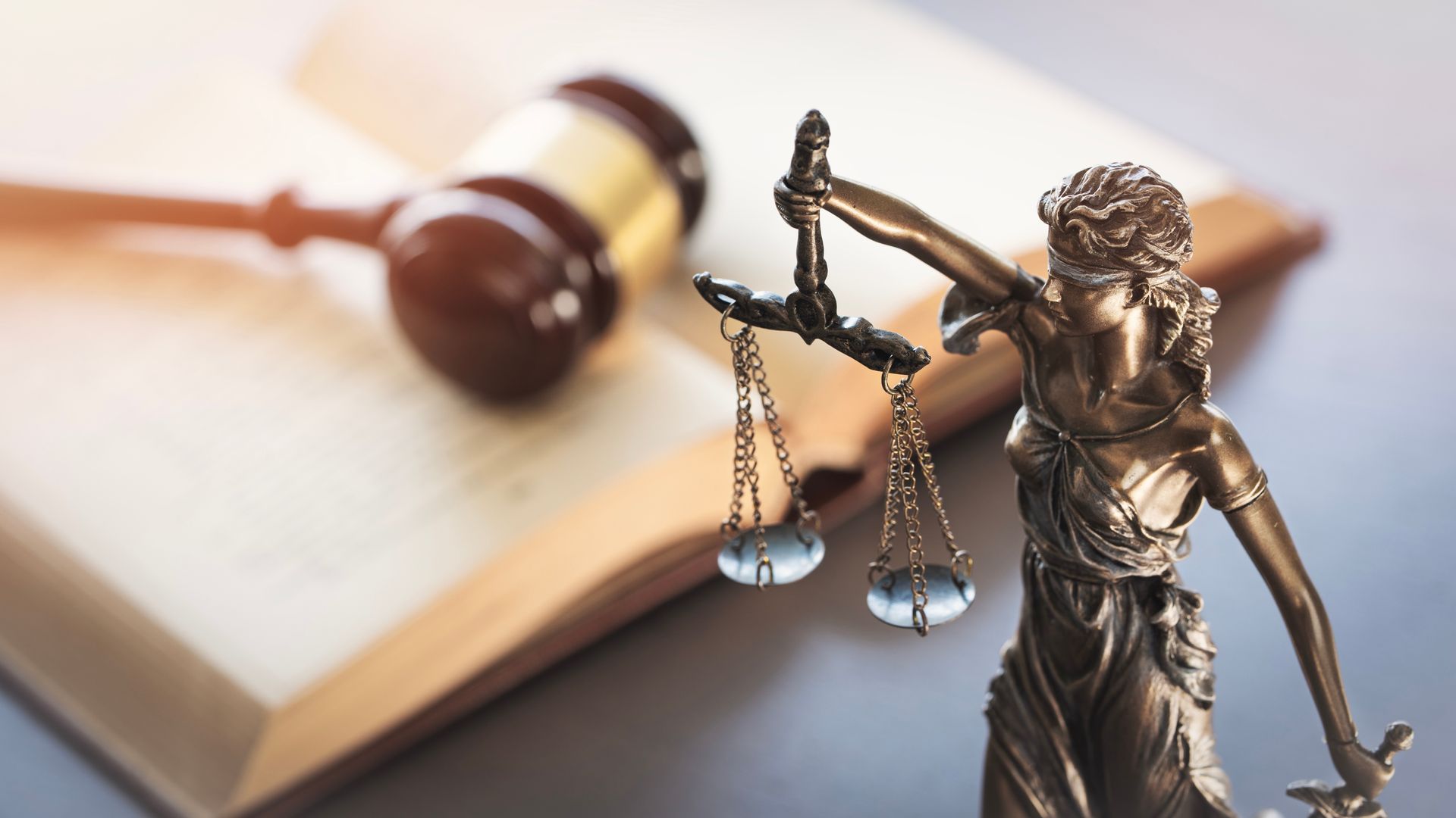 Statue of Lady Justice with scales in front of a blurred law book and gavel