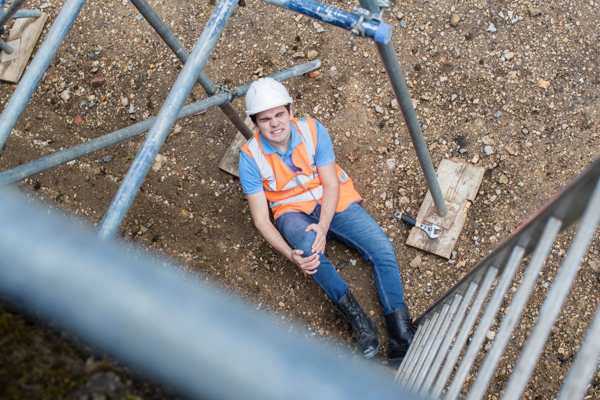 Construction worker in hard hat and orange vest sitting on a ladder, seen from above at a work site