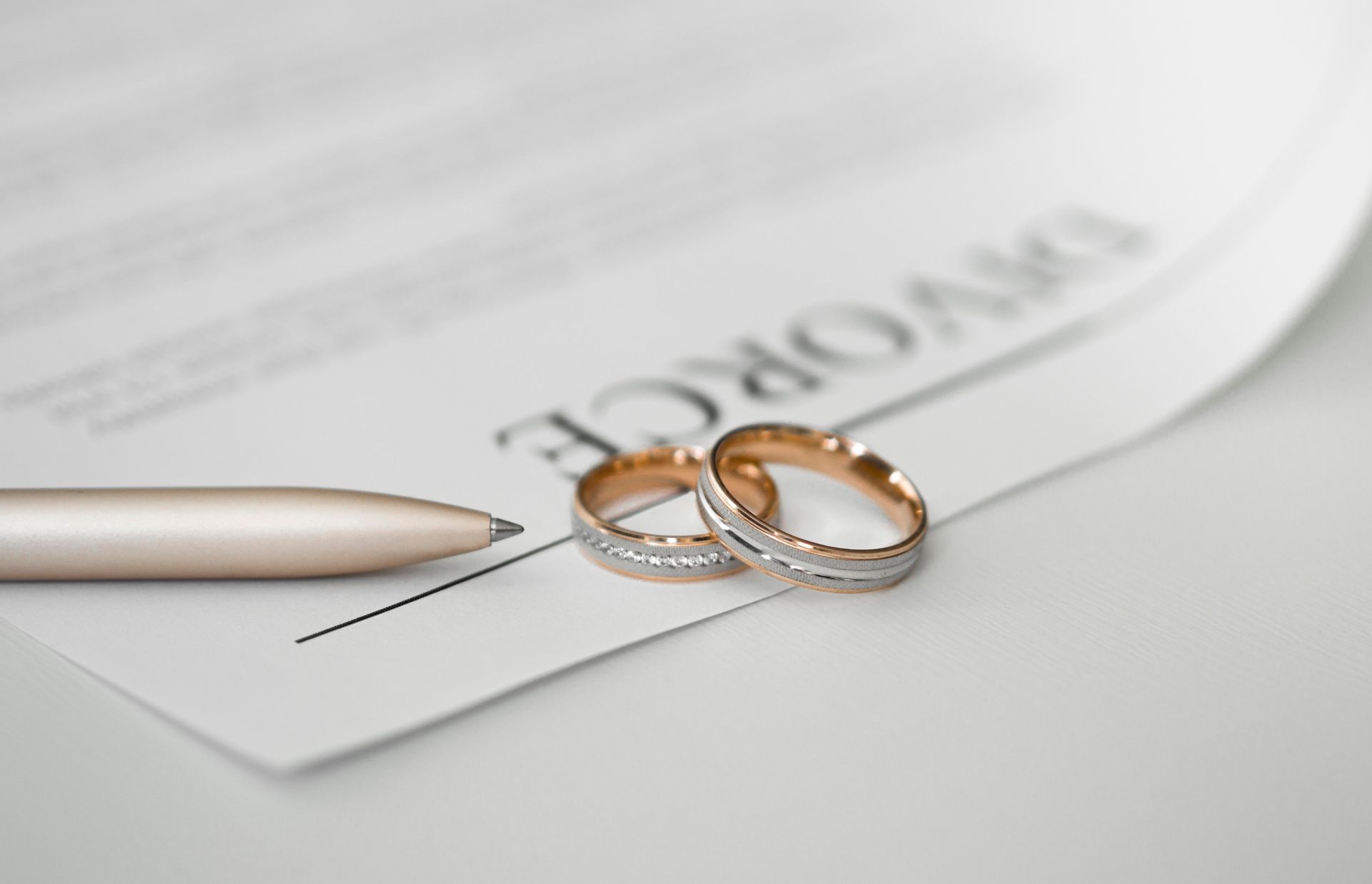 Two wedding rings on a divorce document with a pen.