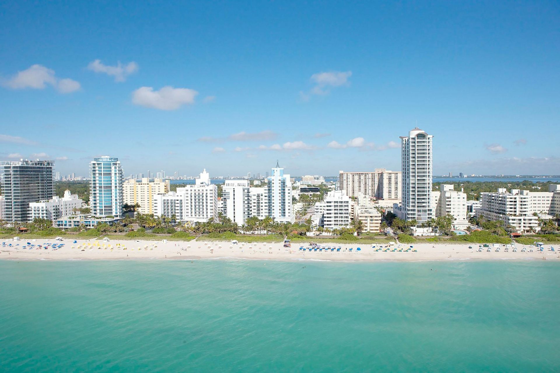 Beachfront view of Miami, Florida, with turquoise water, sandy beach, and buildings under a blue sky.