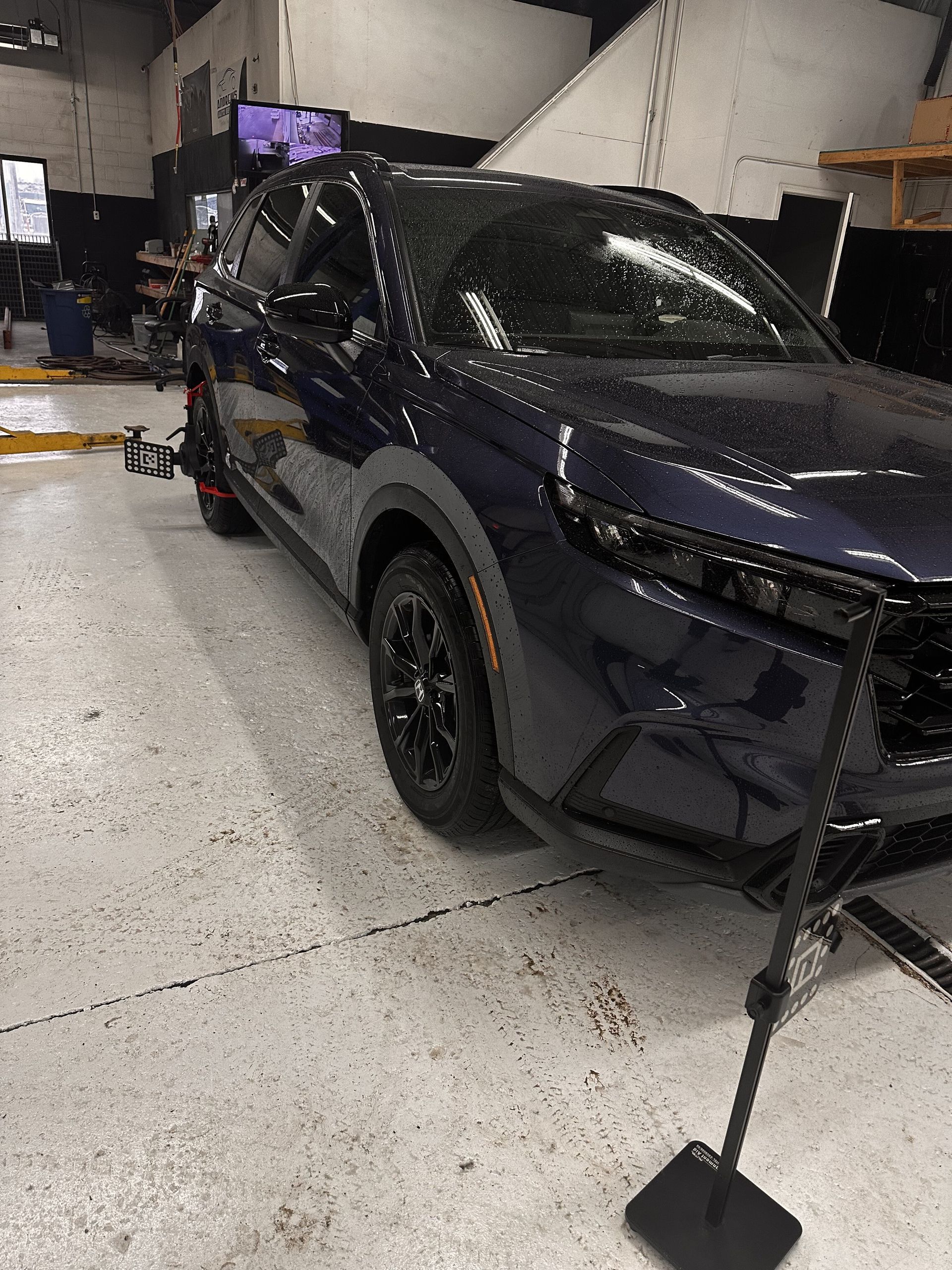 Blue SUV on a lift, in a garage, being aligned with black equipment. | West Michigan A.D.A.S