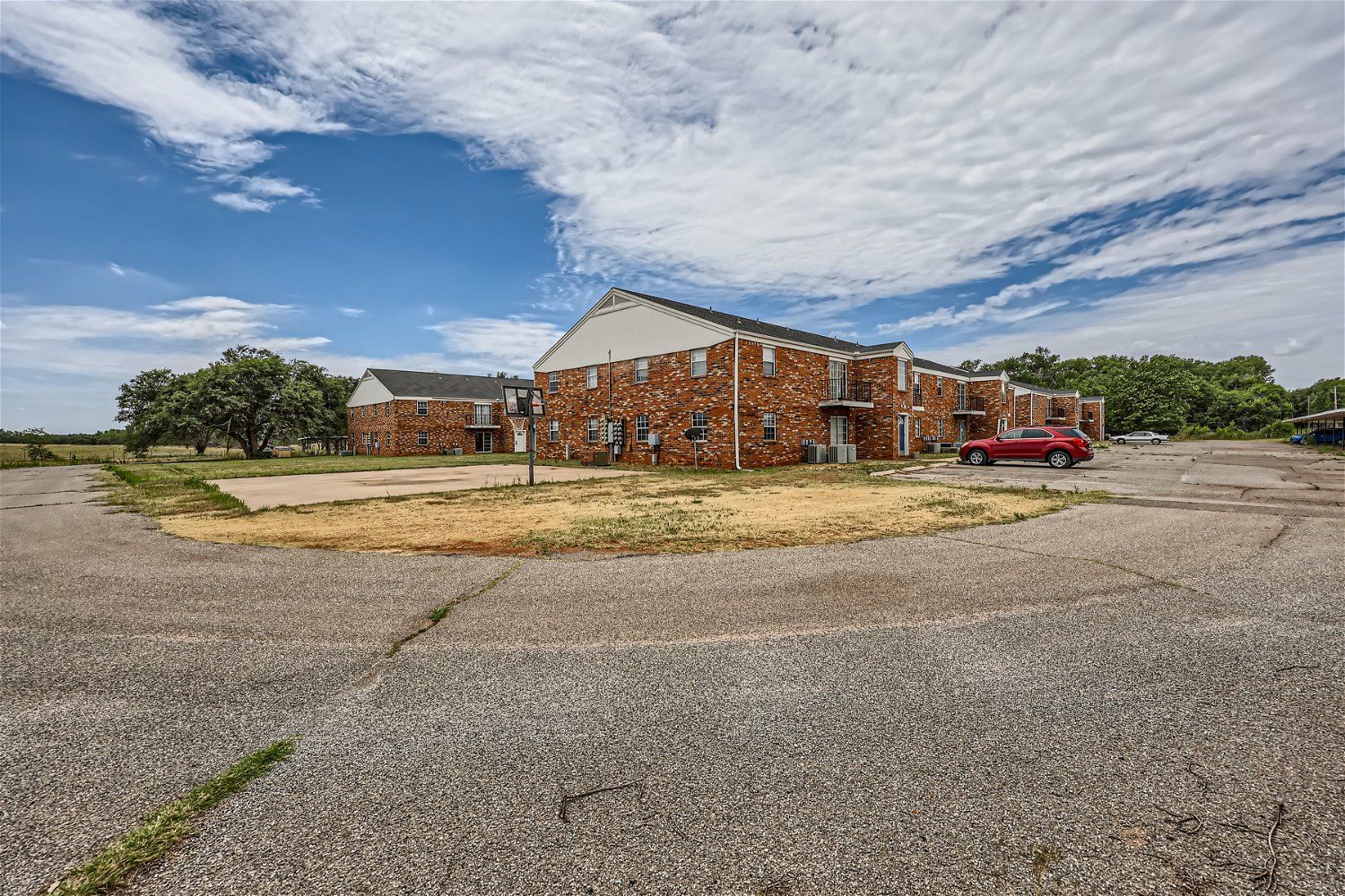 Apartment buildings with brown brick exterior on a cracked, grey asphalt lot under a blue sky.
