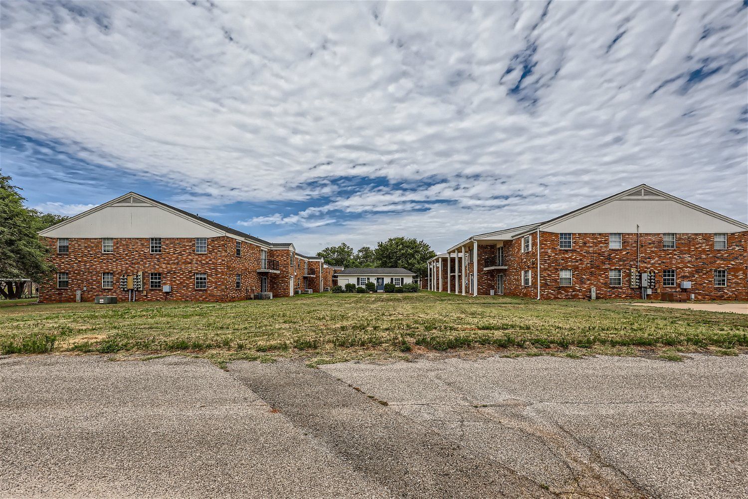 Two brick apartment buildings and a small white building under a cloudy sky.