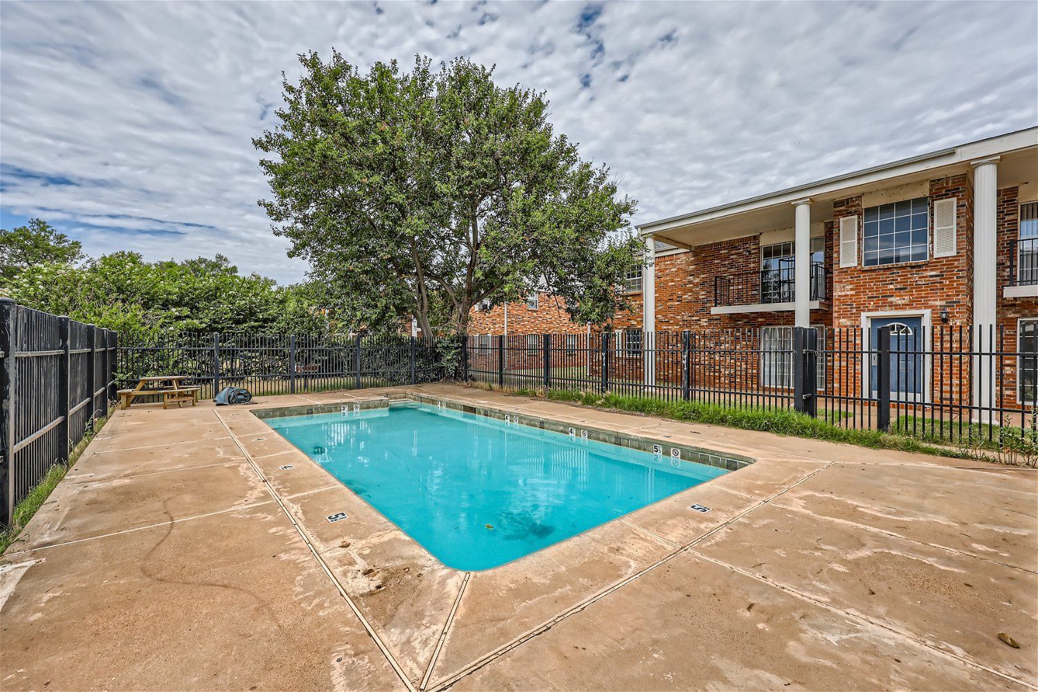 Swimming pool in a brick apartment complex courtyard, surrounded by a black fence.