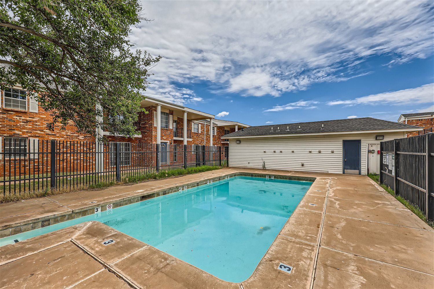 Outdoor swimming pool in front of an apartment building under a cloudy sky.
