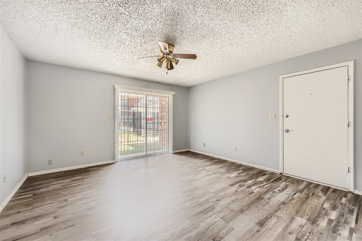 Empty living room with light gray walls, sliding glass door, white door, ceiling fan, and wood-look flooring.