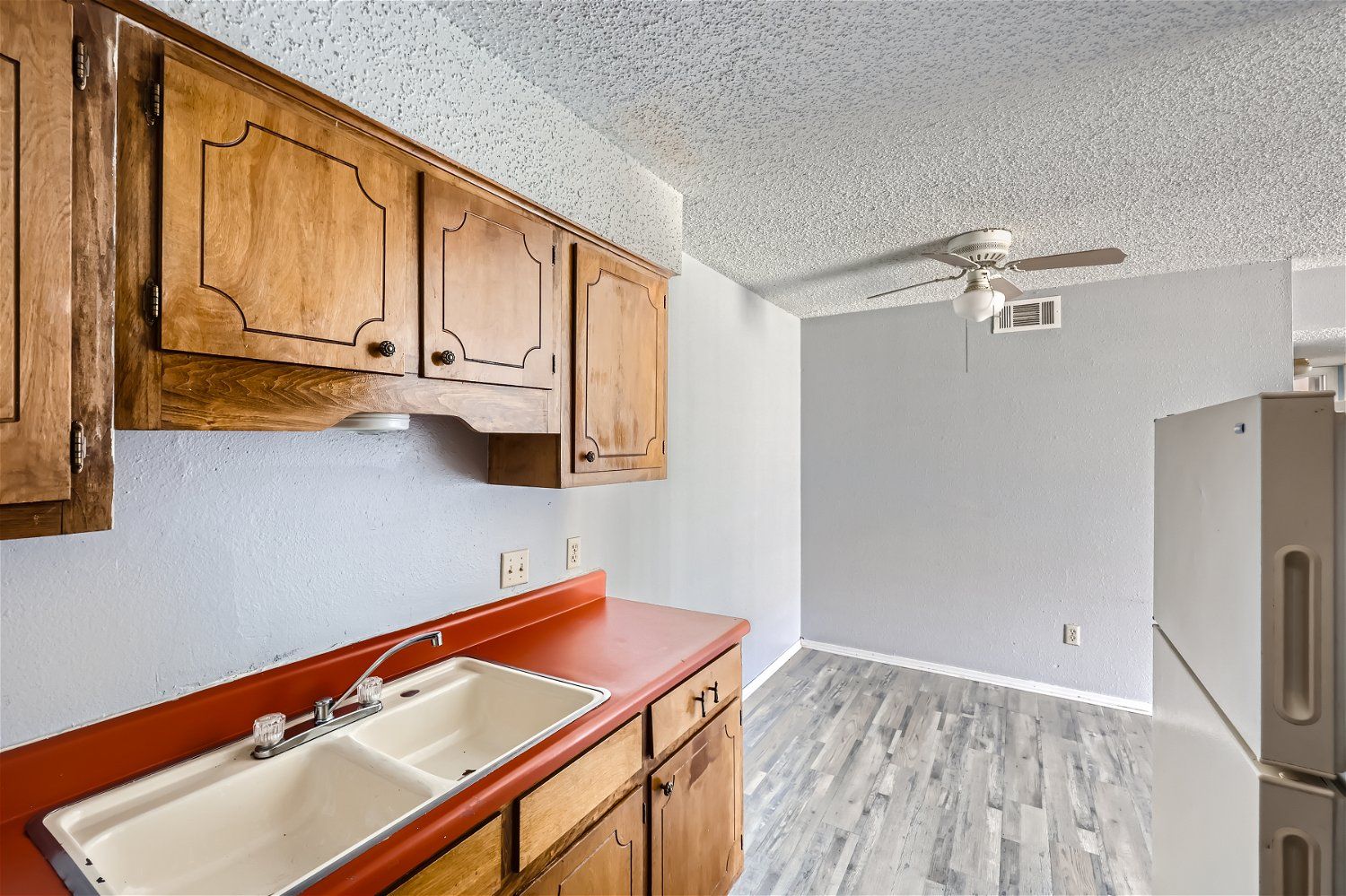 Kitchen with wooden cabinets, red countertop, white sink, and light gray flooring.