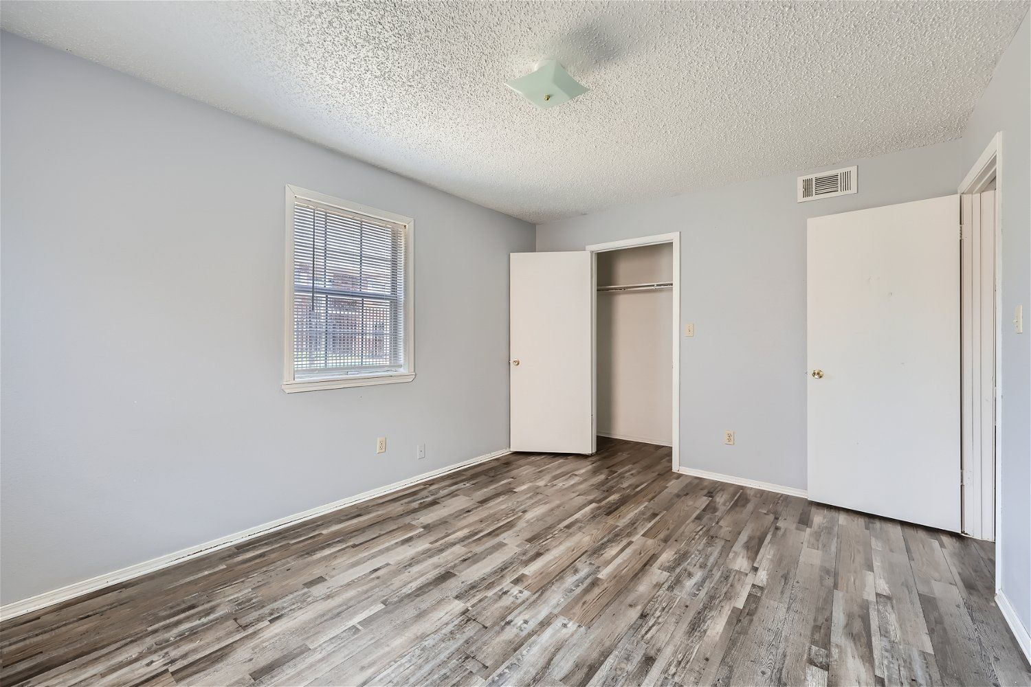 Empty bedroom with gray walls, wood-look flooring, and a white ceiling with a light fixture.