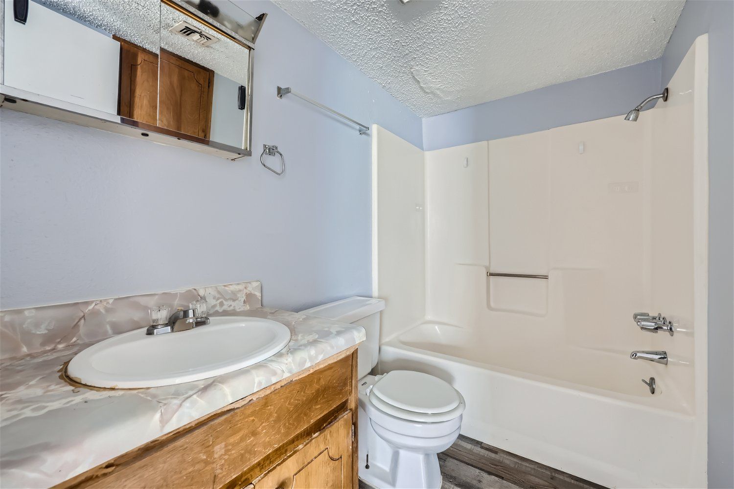 Bathroom with a white bathtub, toilet, and sink, light blue walls, and a wooden cabinet.