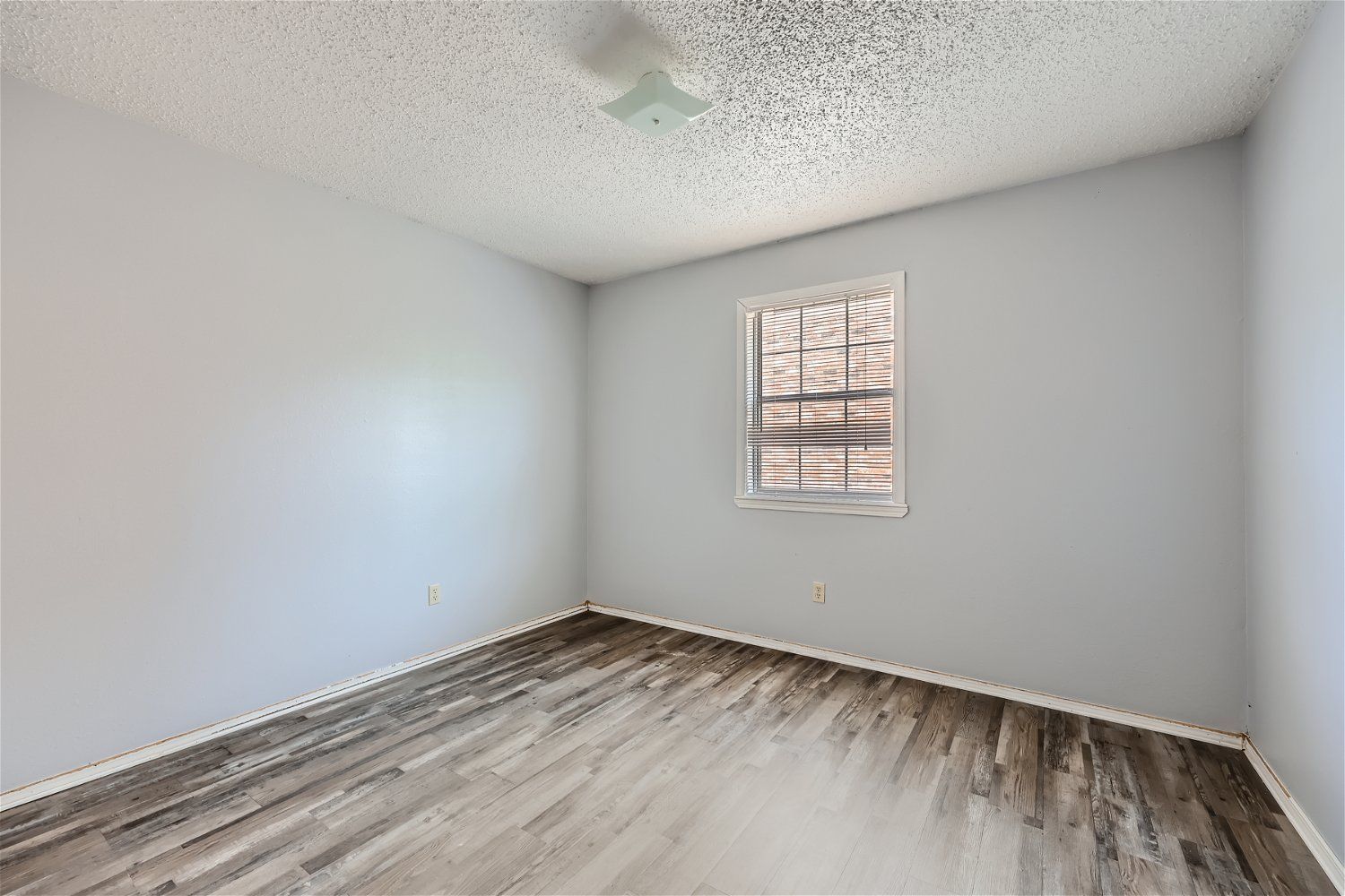 Empty room with gray walls, wood-look flooring, and a window.