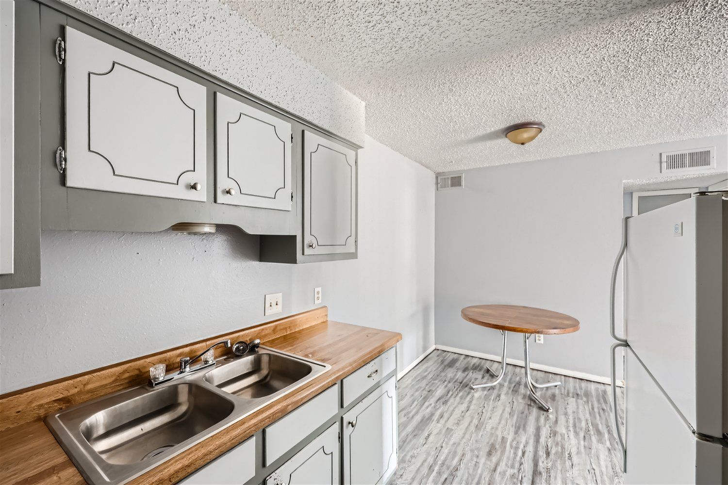 Small kitchen with gray cabinets, wooden countertops, stainless steel sink, and a round table.