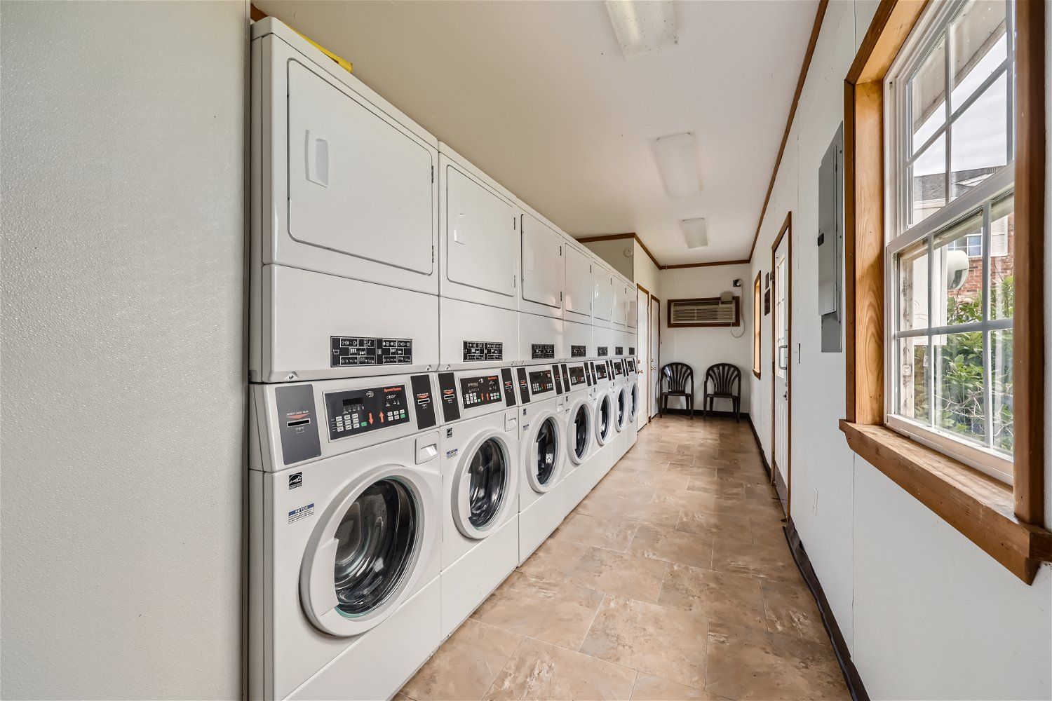 Laundry room with multiple washers and dryers along a wall. Window on the right.