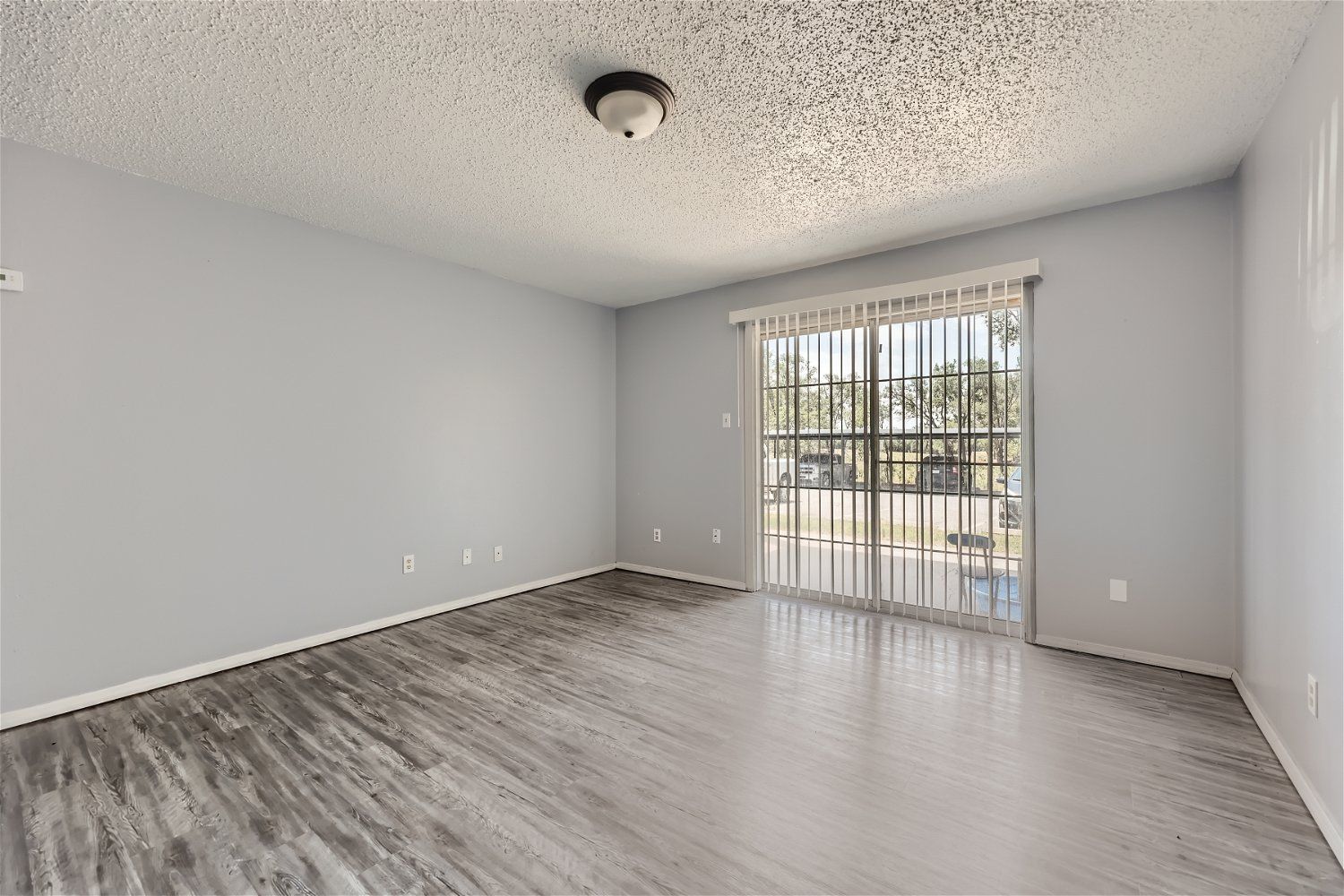 Empty room with gray walls, wood-look floor, and sliding glass door.
