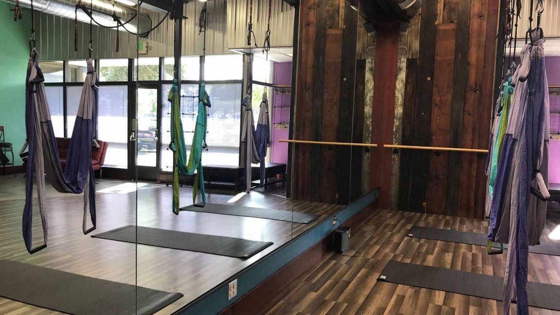 Suspended yoga hammocks in a studio with mats, windows, and wooden flooring