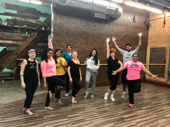 Group dancing in a studio, with one person leading and others following in colorful workout clothes.