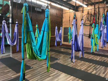 Colorful aerial yoga hammocks hanging in a studio with mats on the floor