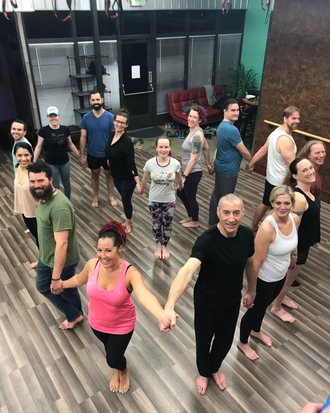 People standing in a dance studio, holding hands in a line on a wood floor.