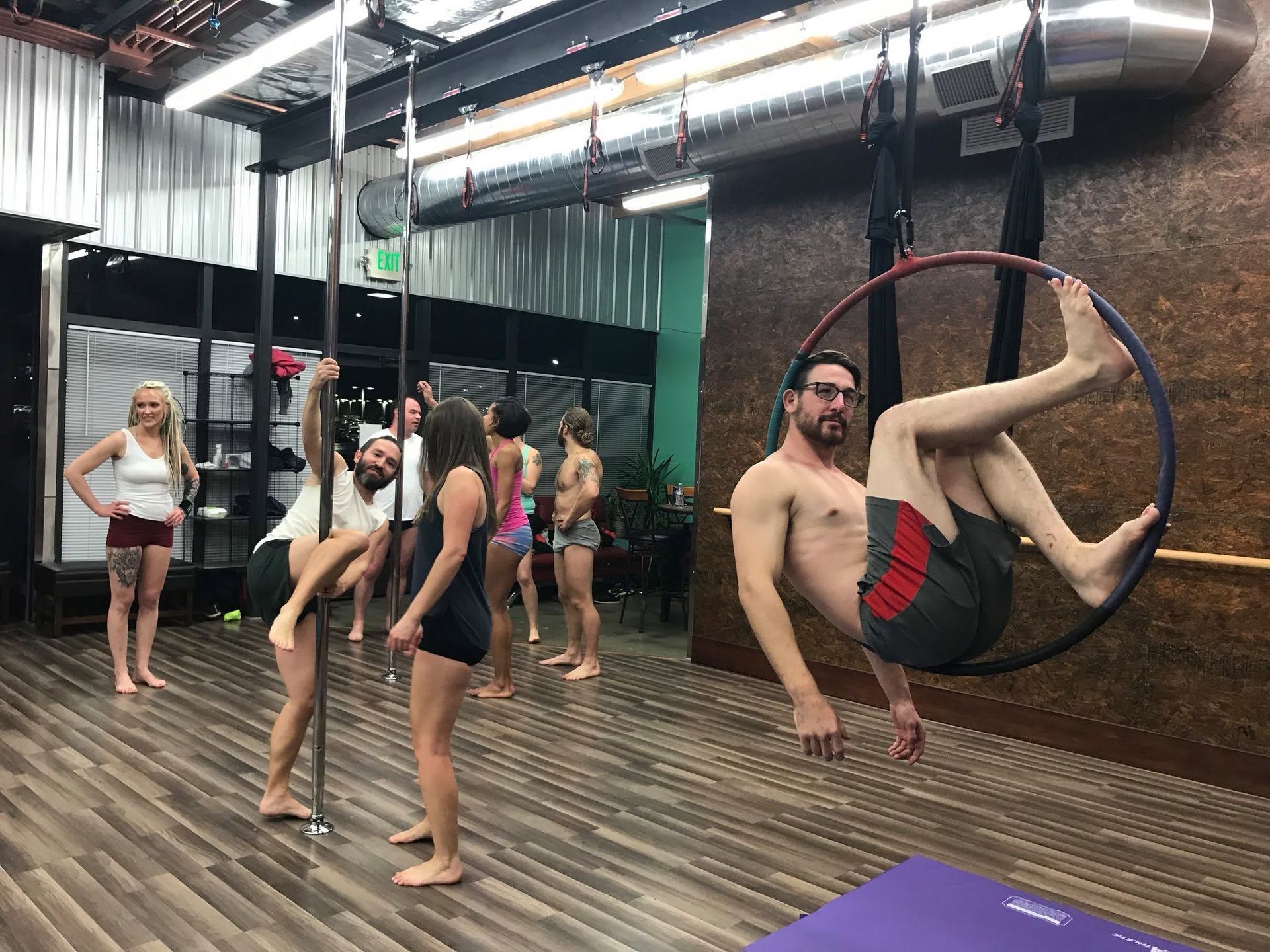 Aerial hoop class in a studio, with a man performing on a hoop and others standing nearby.