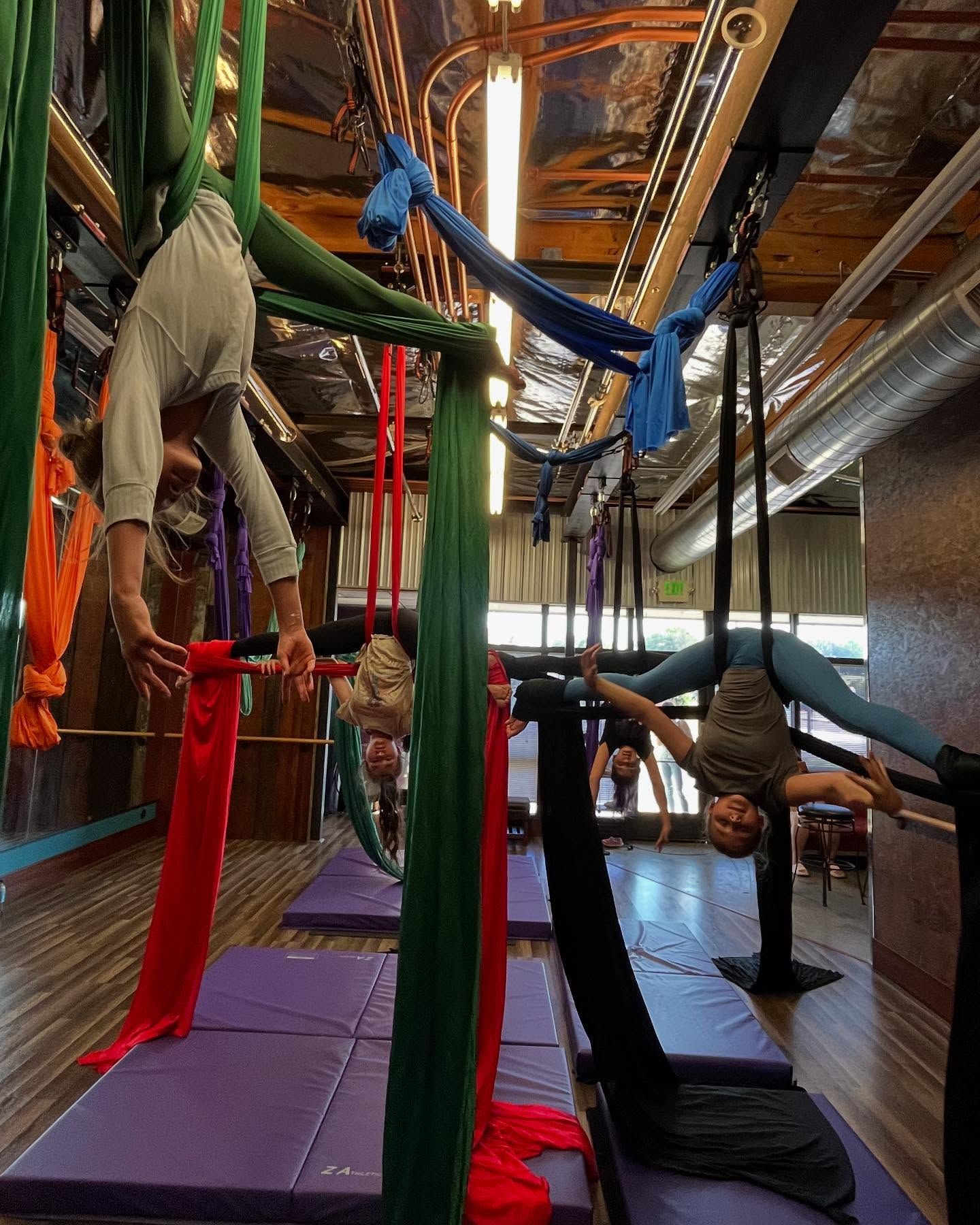 People doing aerial yoga on colorful silks in a studio