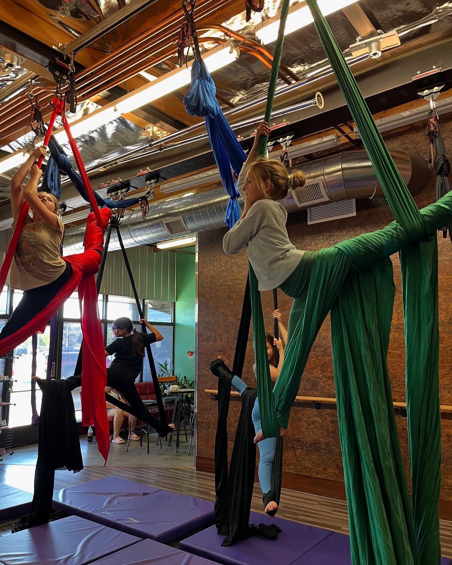 People hanging and stretching from colorful aerial silks in a studio class