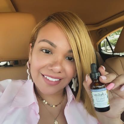 Woman in car holds a small brown bottle with a dropper; she is smiling. Level Up Falcon
