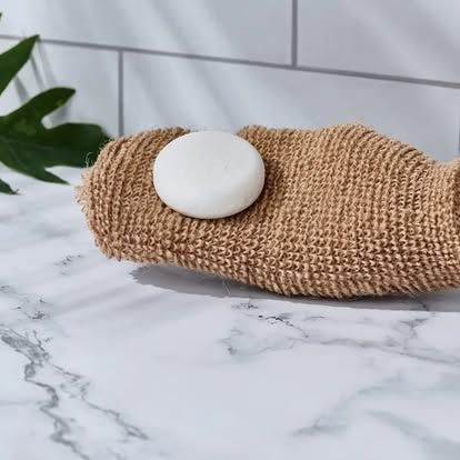 A round white soap bar rests on a brown textured mitt on a marble countertop. Level Up Falcon