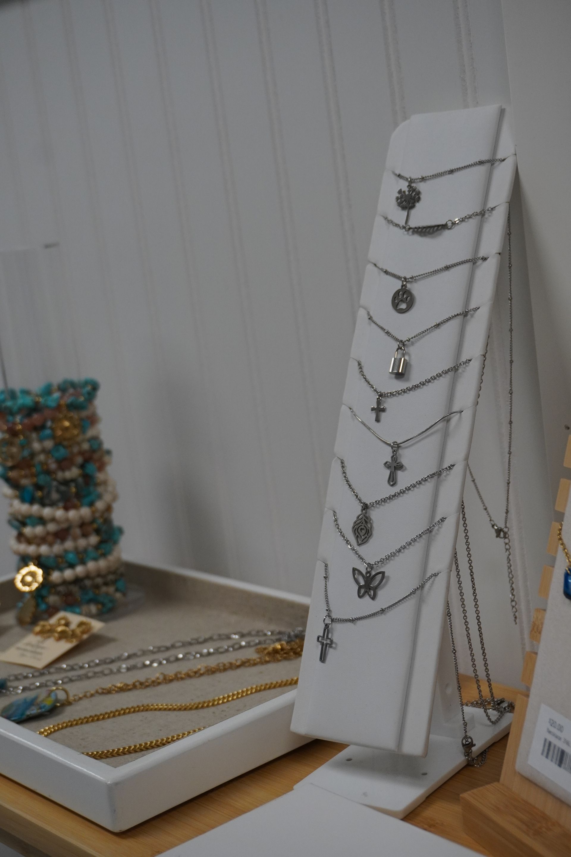 Jewelry display: necklaces on a white stand, bracelets in a tray. Wooden table against a white wall. Level Up Falcon