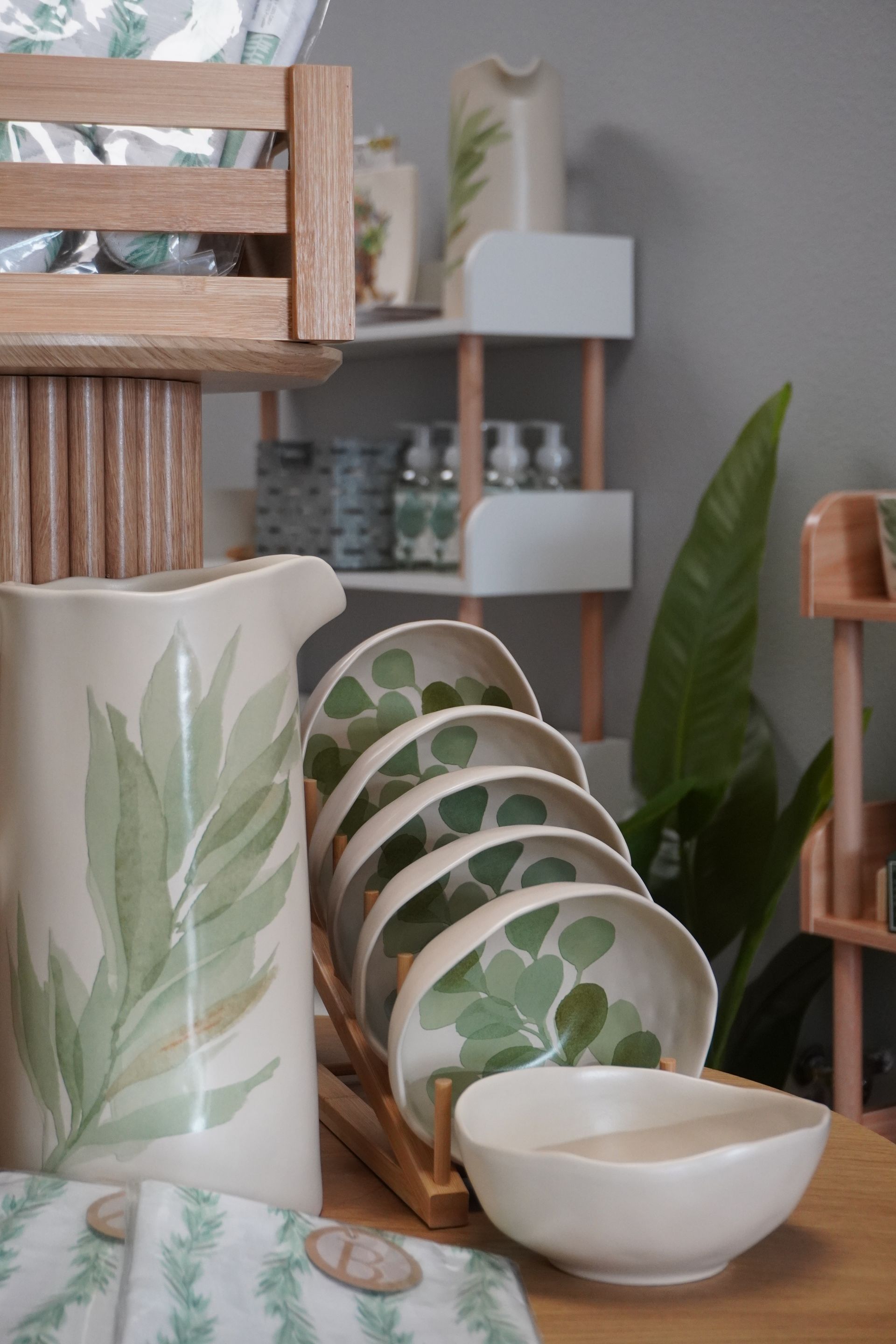 Ceramic pitcher and bowls with green leaf designs, displayed with wooden shelves and a leafy plant. Level Up Falcon