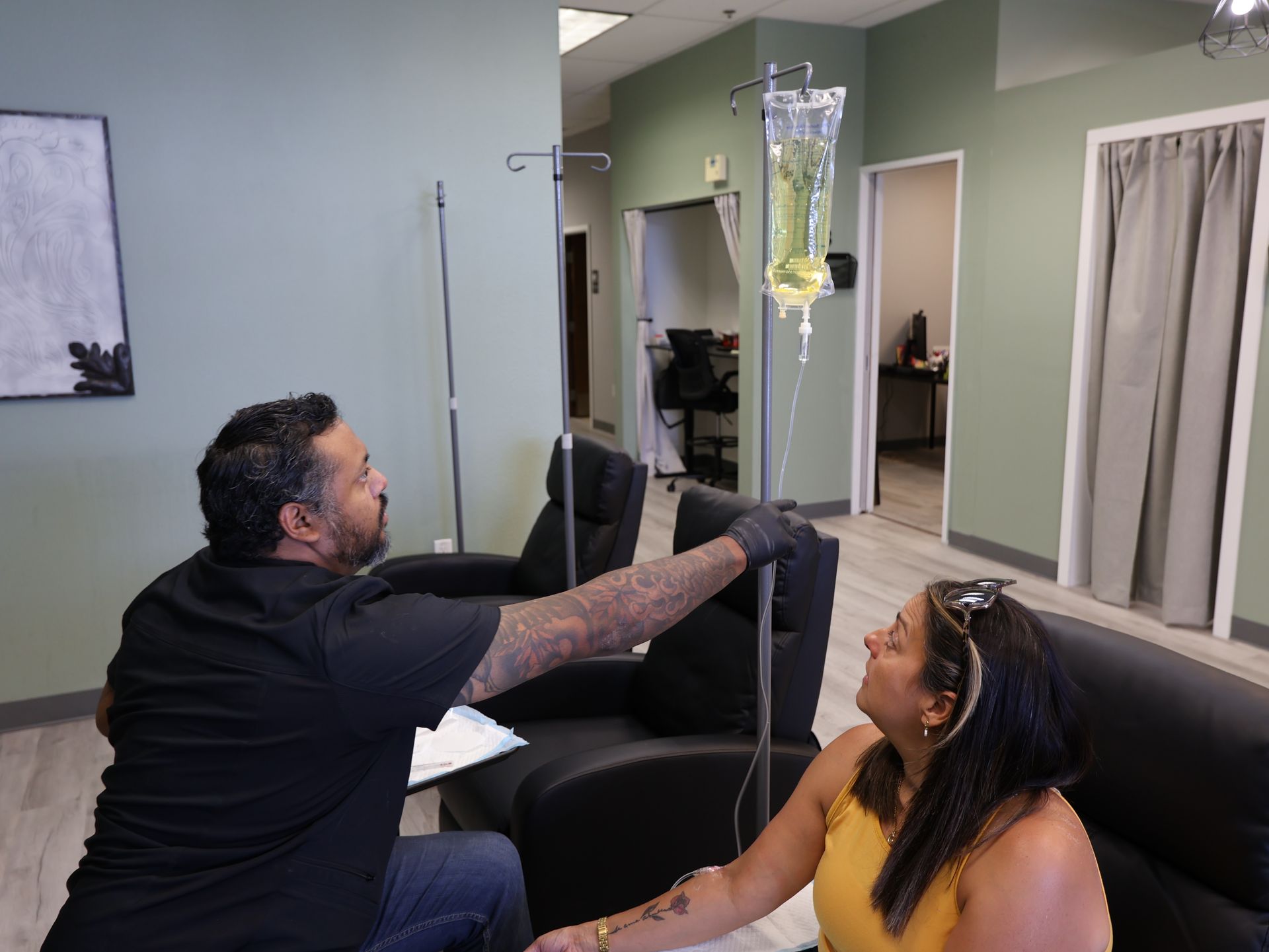 A person receiving IV fluids in a medical setting. A healthcare worker is preparing the equipment. Level Up Falcon