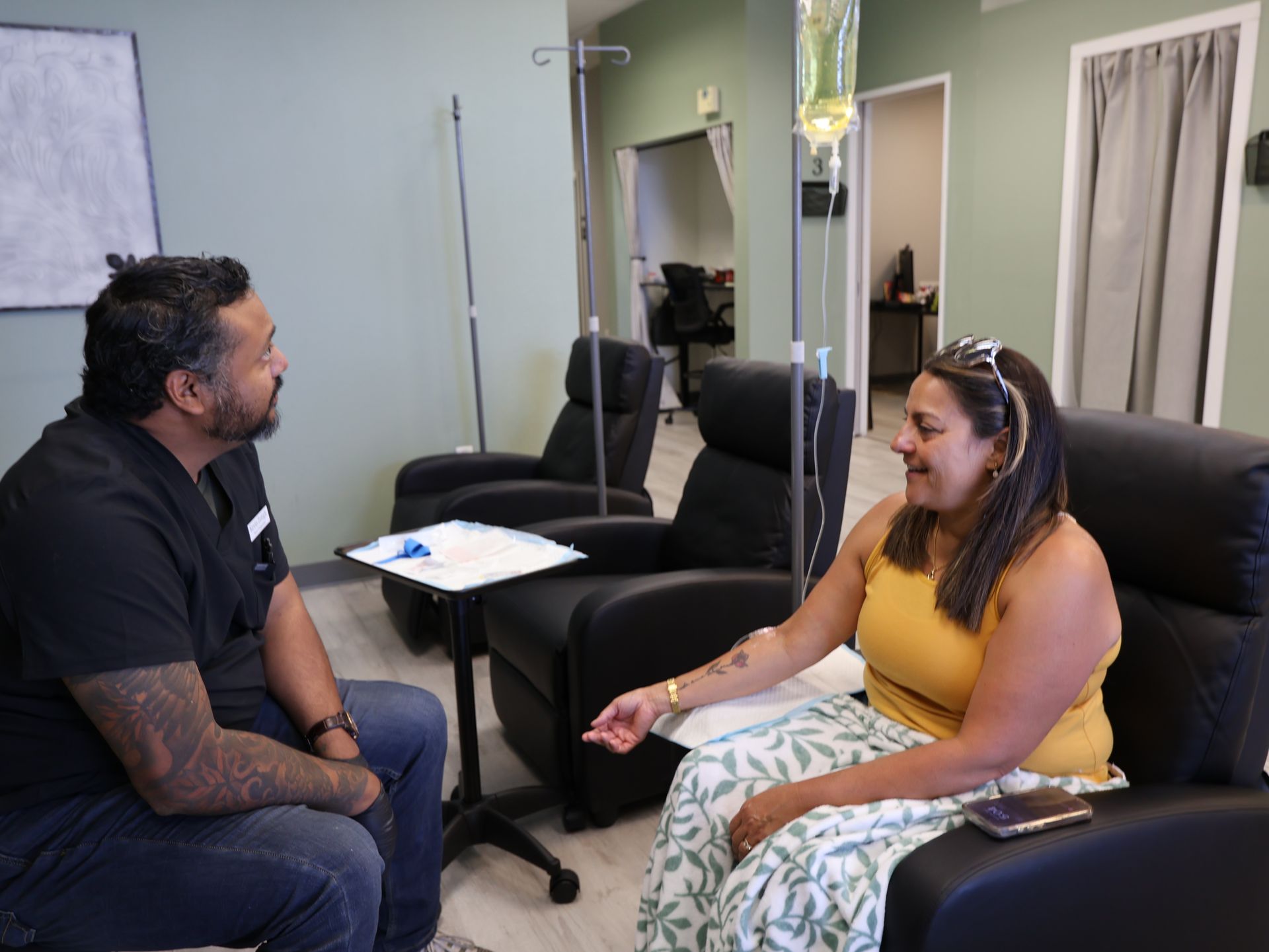 Man talking to woman seated in a chair with an IV drip in a medical office. Level Up Falcon