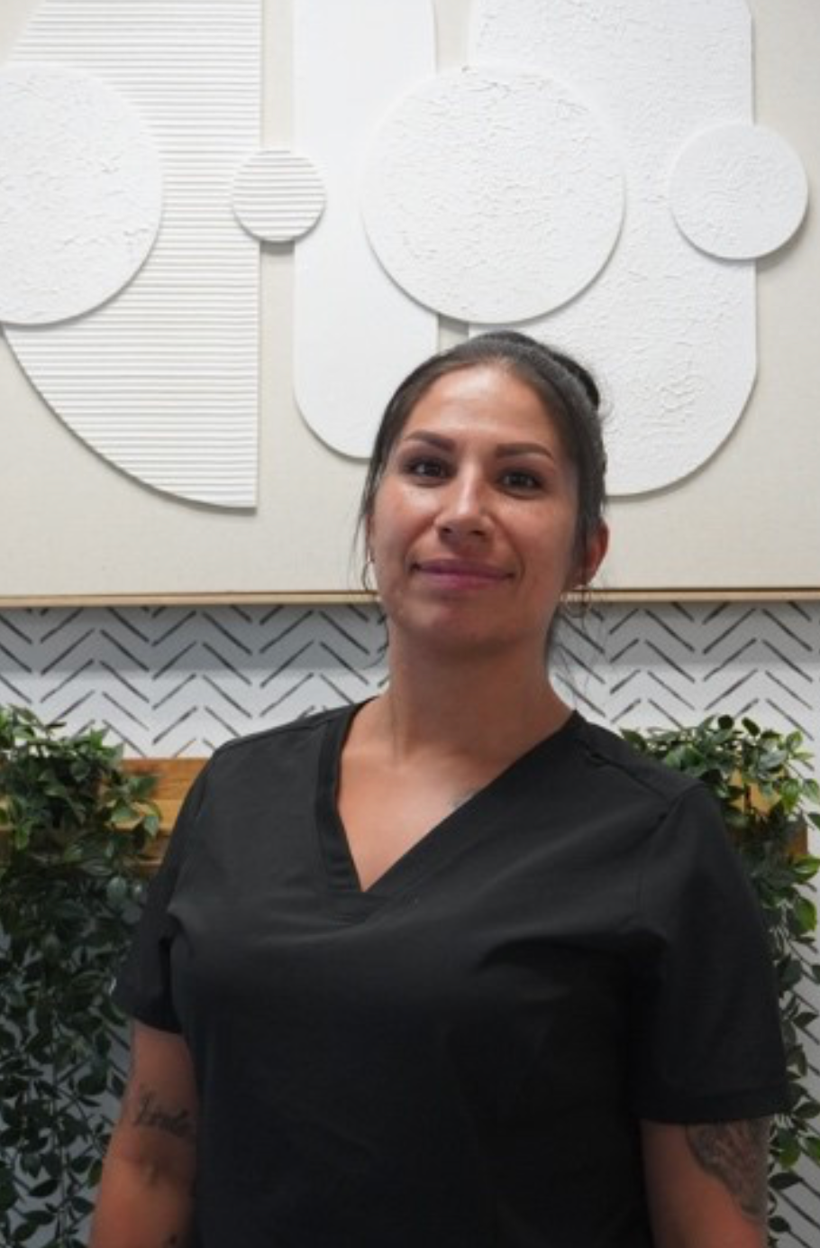 Woman in black scrubs, smiling, standing in front of white wall art and greenery. Level Up Falcon