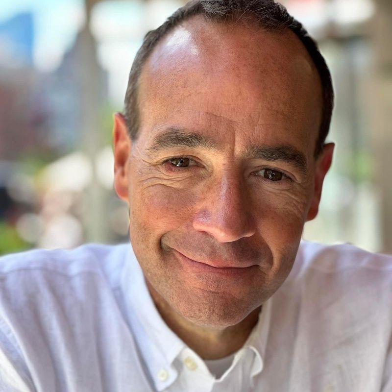 A man in a suit and white shirt is smiling for the camera.